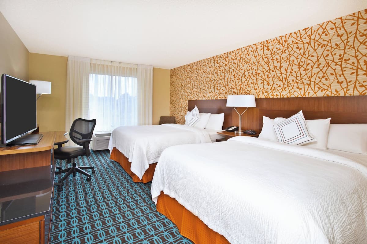 Ein Hotelzimmer mit zwei Betten, einem Schreibtisch mit Computer, einem Sessel und einem Fernseher.
