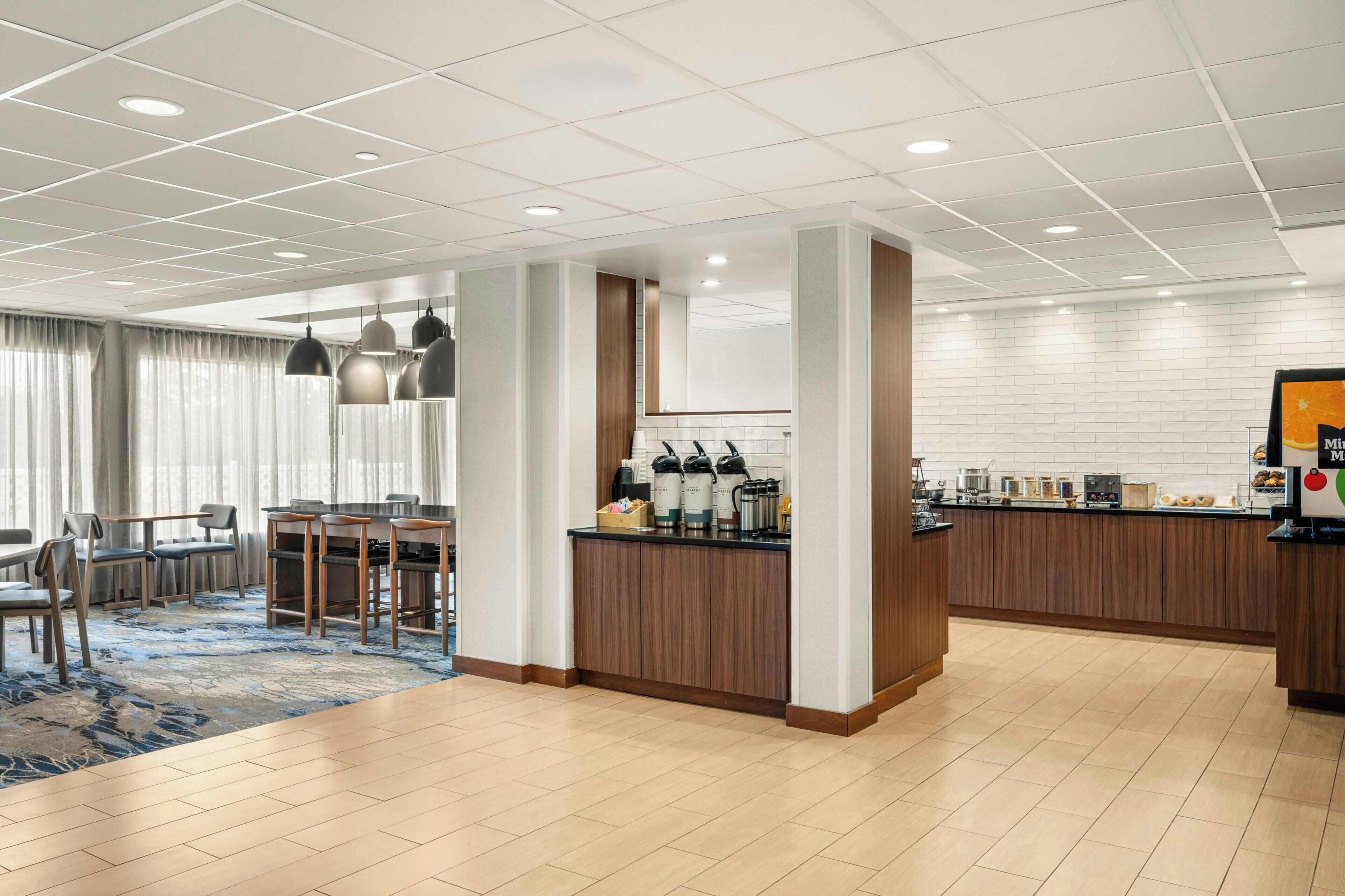 Un hall d’hôtel moderne comprenant un espace repas, un bar et un comptoir de cuisine.
