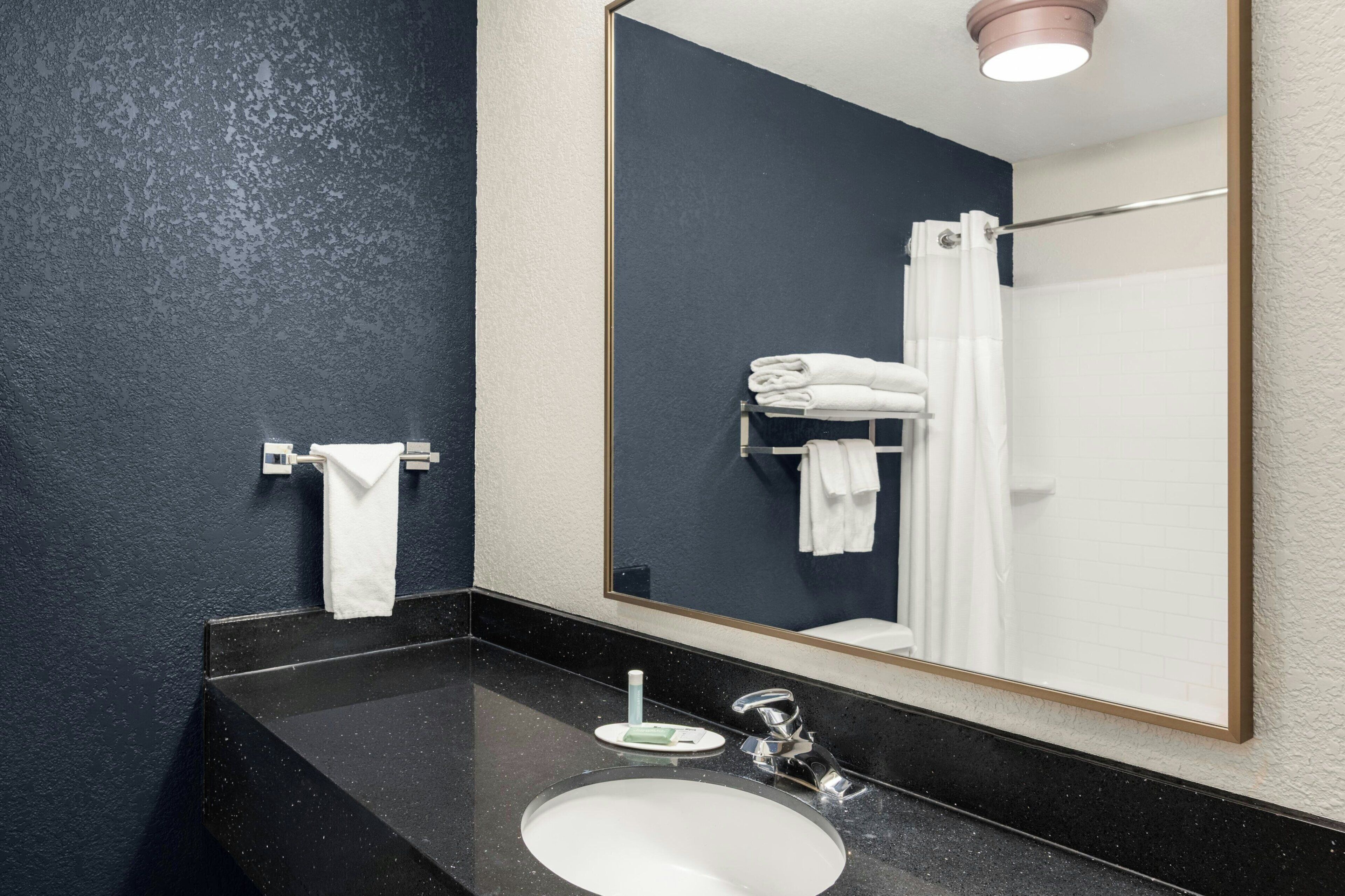 A modern bathroom with a black countertop, a white sink, a large mirror, and a towel rack.