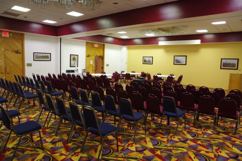 A conference room with rows of blue chairs, a patterned carpet, and yellow walls.