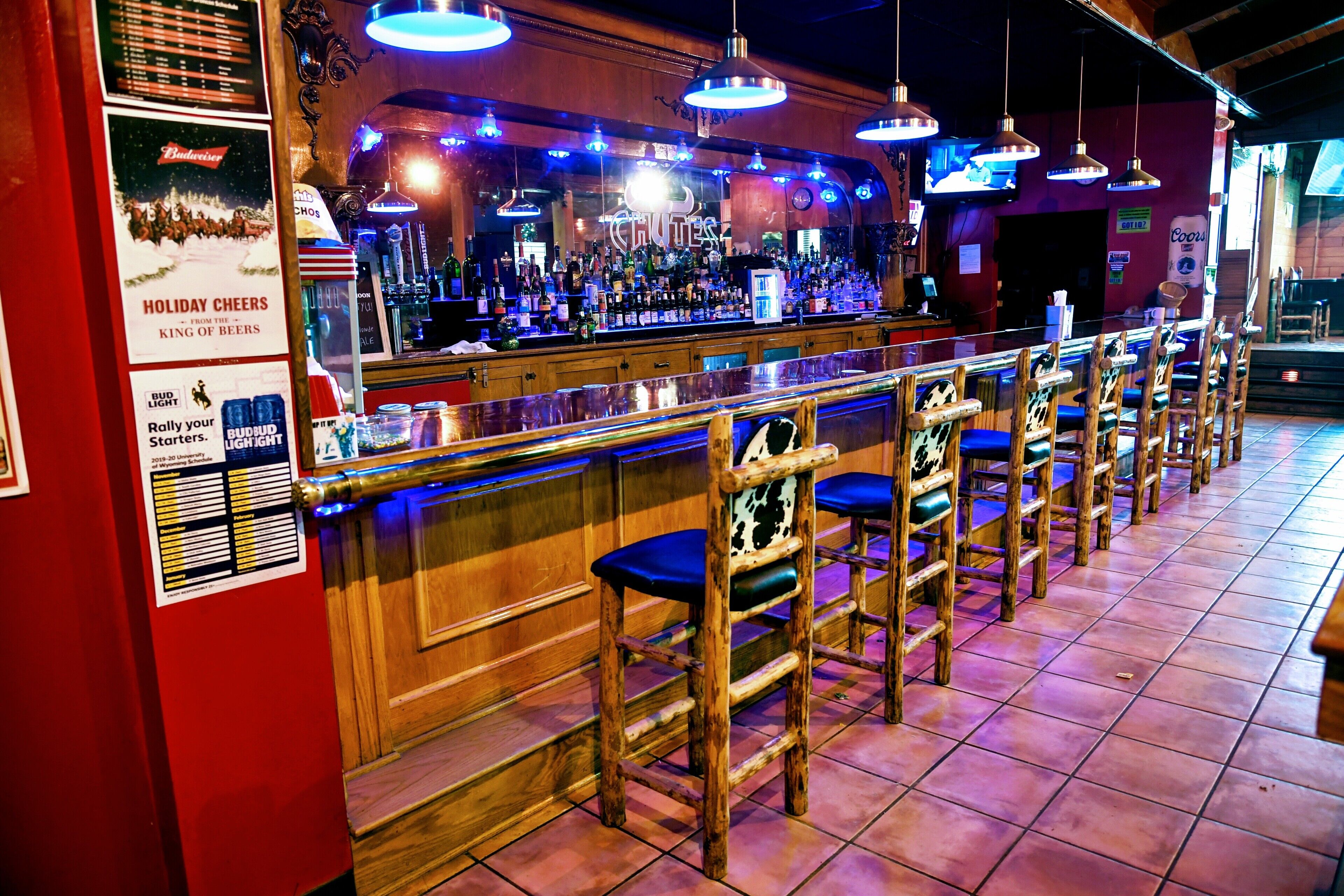 Zona de bar con mostradores y taburetes de madera, una variedad de botellas y un letrero con motivos navideños.