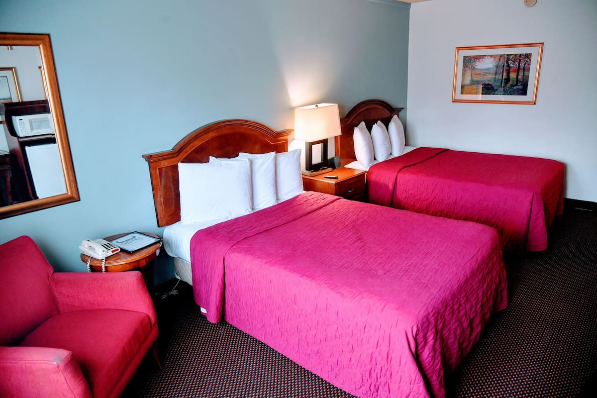 Ein Hotelzimmer mit zwei Betten, einem roten Sessel, einem Nachttisch mit Lampe, einem Telefon und einem Bild an der Wand.
