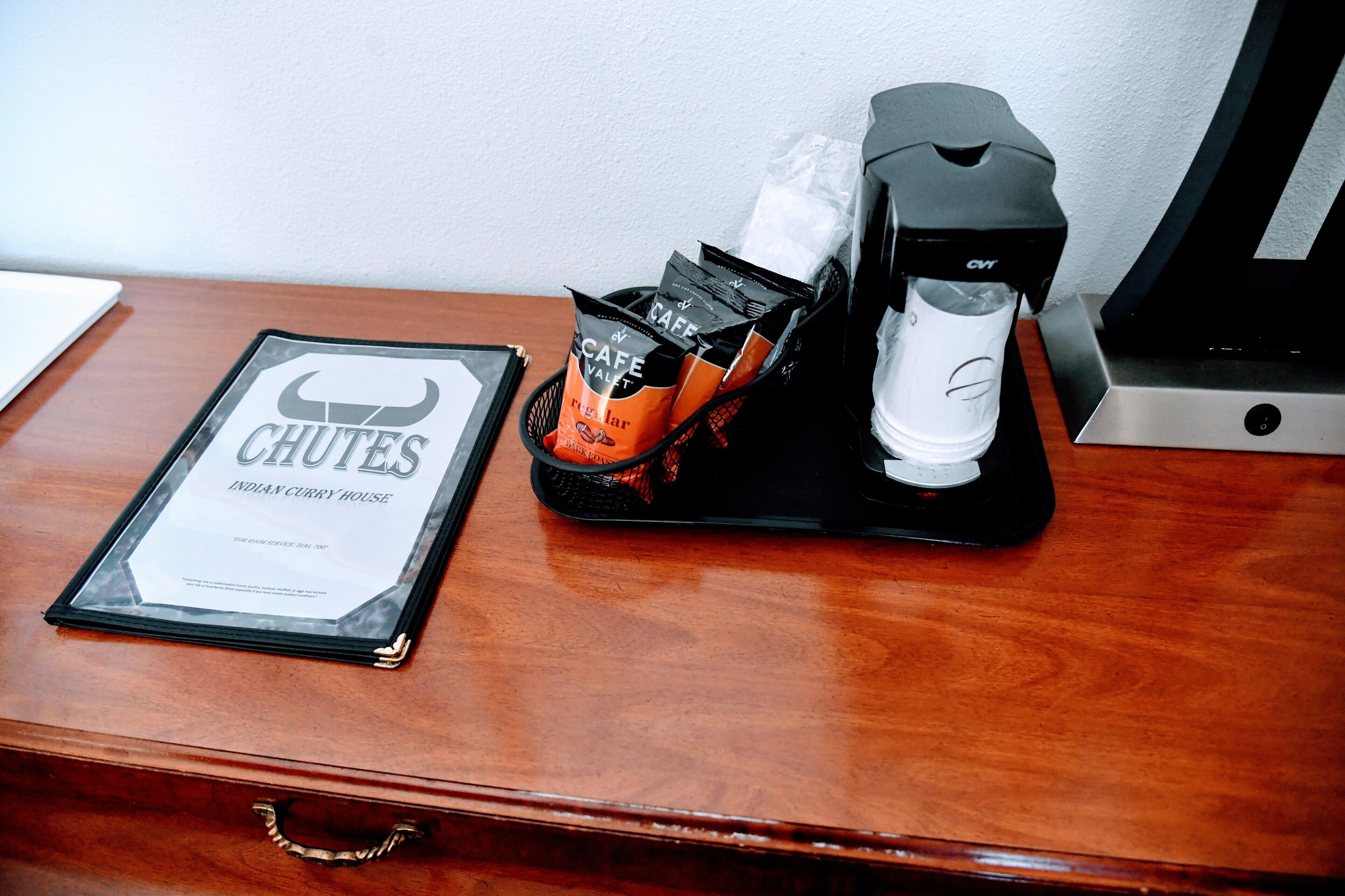 A coffee maker, a basket of coffee pods, and a menu on a wooden table.