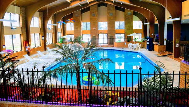 An indoor swimming pool with a high ceiling and arched windows, surrounded by lounge chairs and potted plants. - Douglas Inn & Conference Center (Douglas)