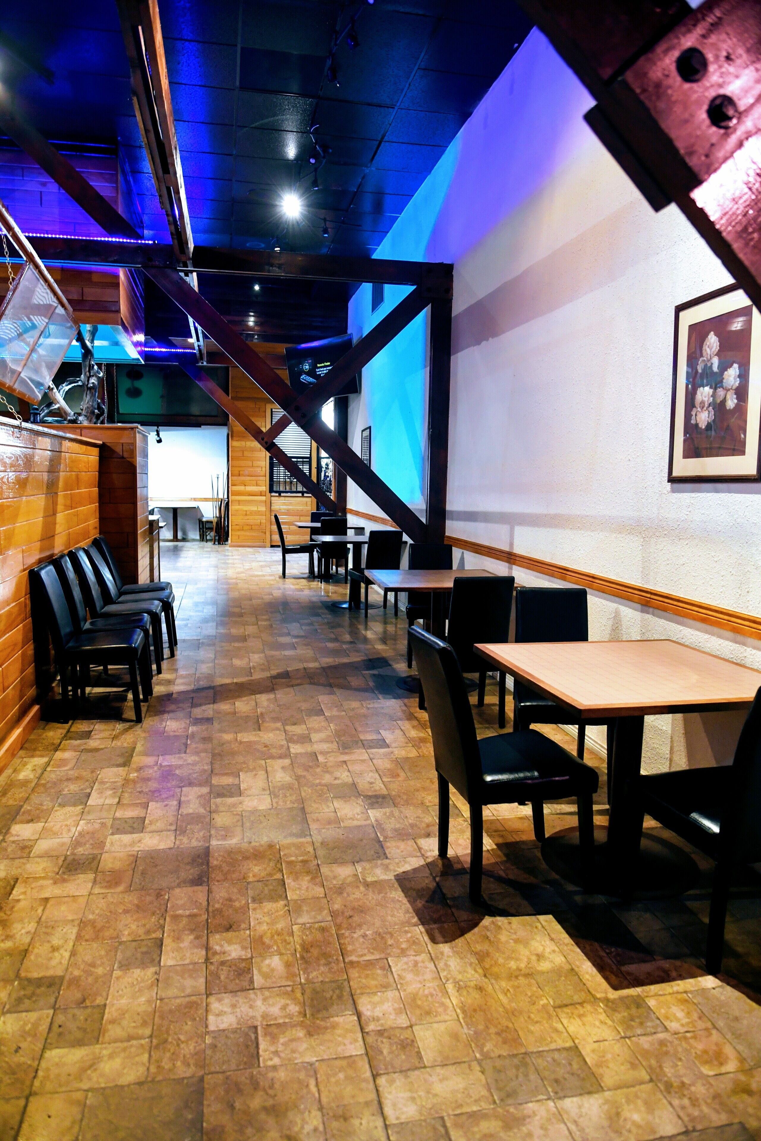 Interior de restaurante com soalho de tijolo, mesas e cadeiras de madeira, e uma escadaria para um andar superior.