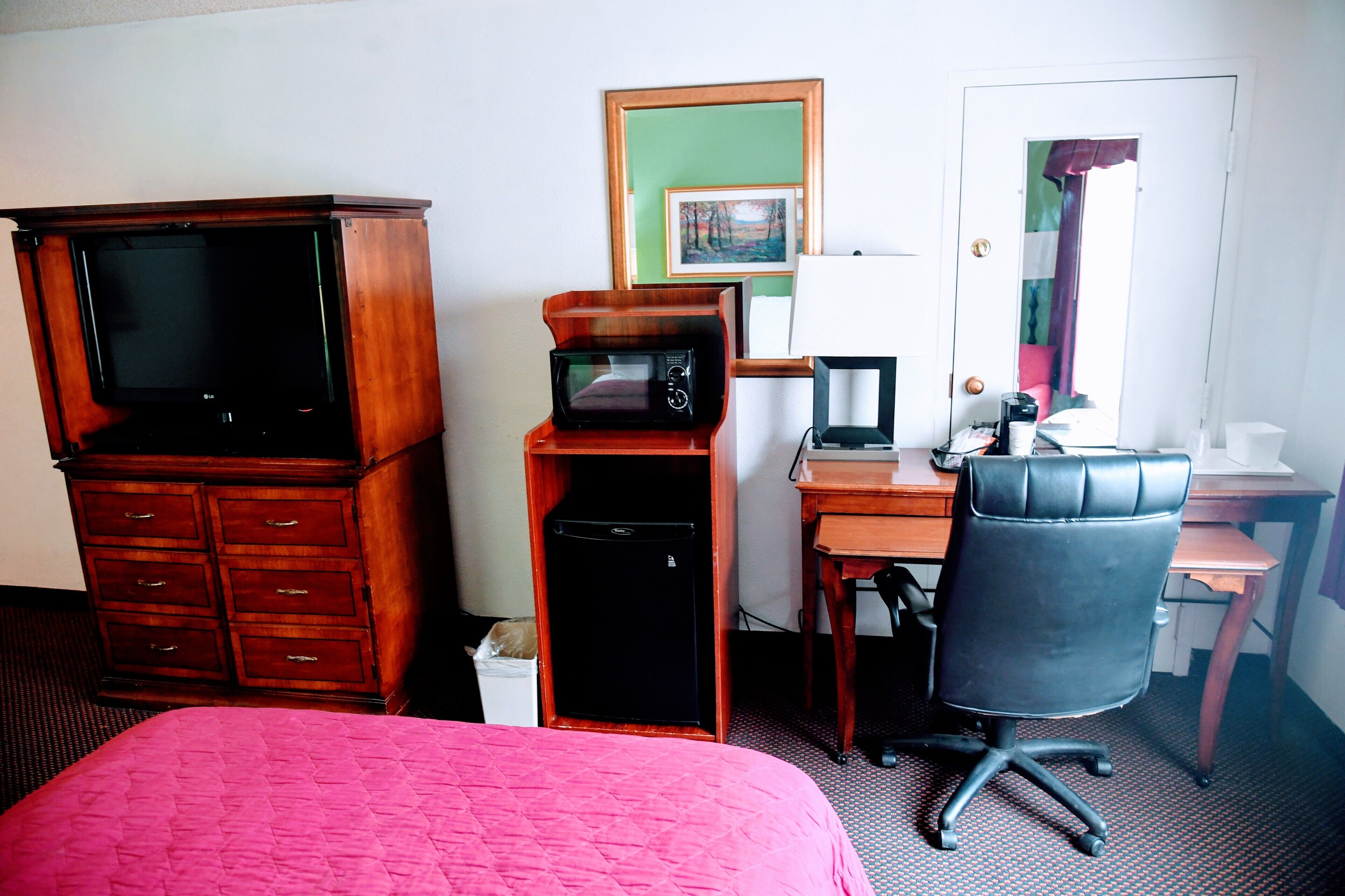 Una habitación de hotel con una cama, un escritorio con computadora, una silla, un microondas y un televisor.