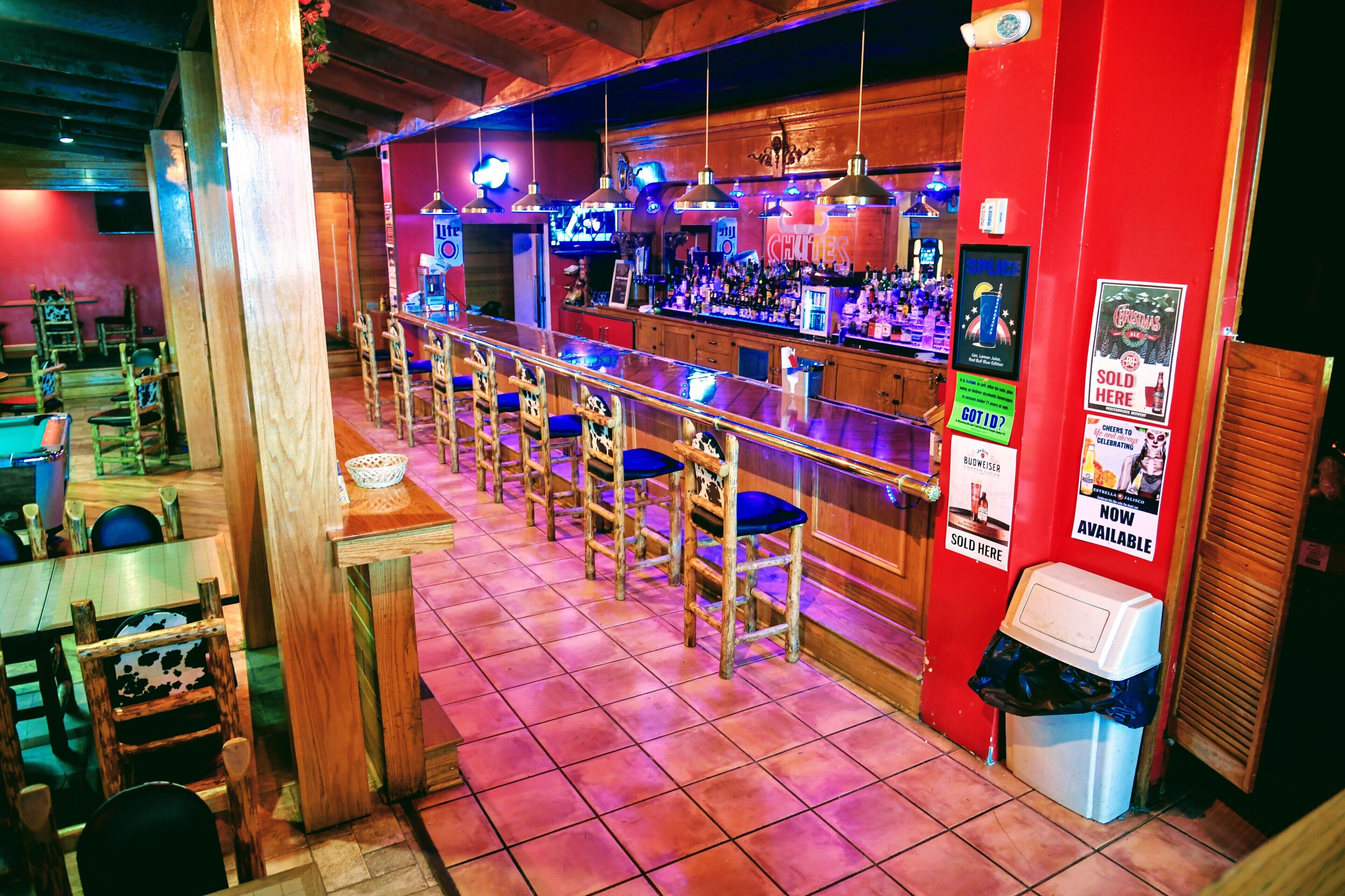 Una zona de bar con sillas de madera y una barra, un cubo de basura y un televisor montado en la pared.