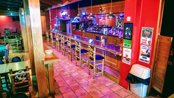 Una zona de bar con sillas de madera y una barra, un cubo de basura y un televisor montado en la pared.
