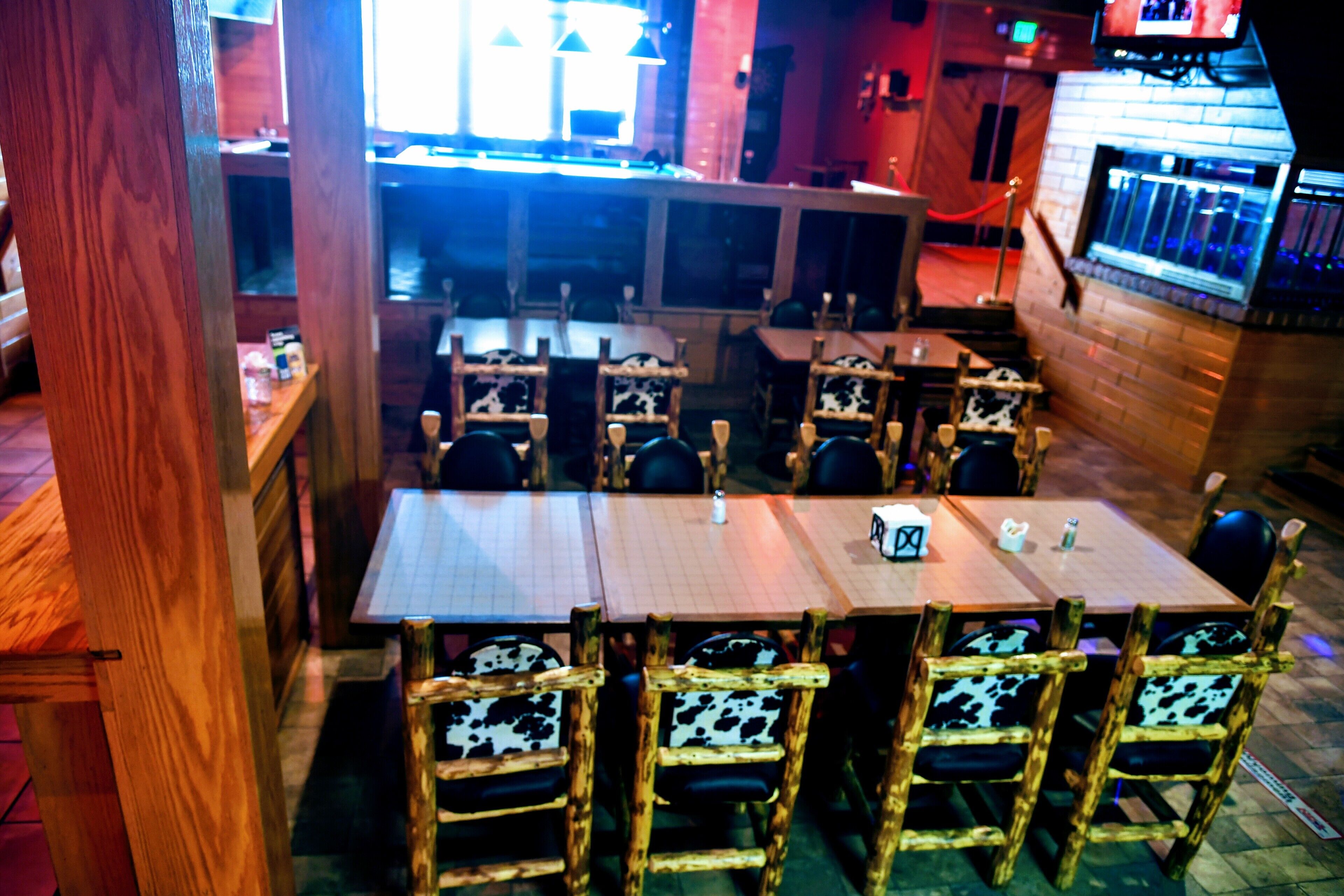 A restaurant with wooden tables and chairs, a bar area, and a view of the street.