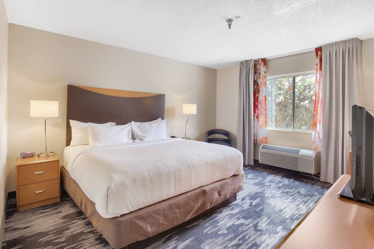 A hotel room with a large bed, bedside lamps, a desk, a chair, and a TV.