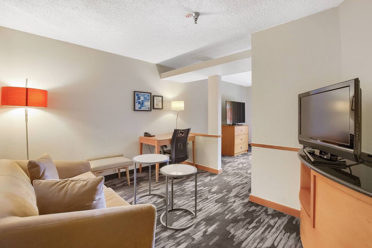 A hotel room with a sofa, two small tables, a TV, a desk, and a chair.