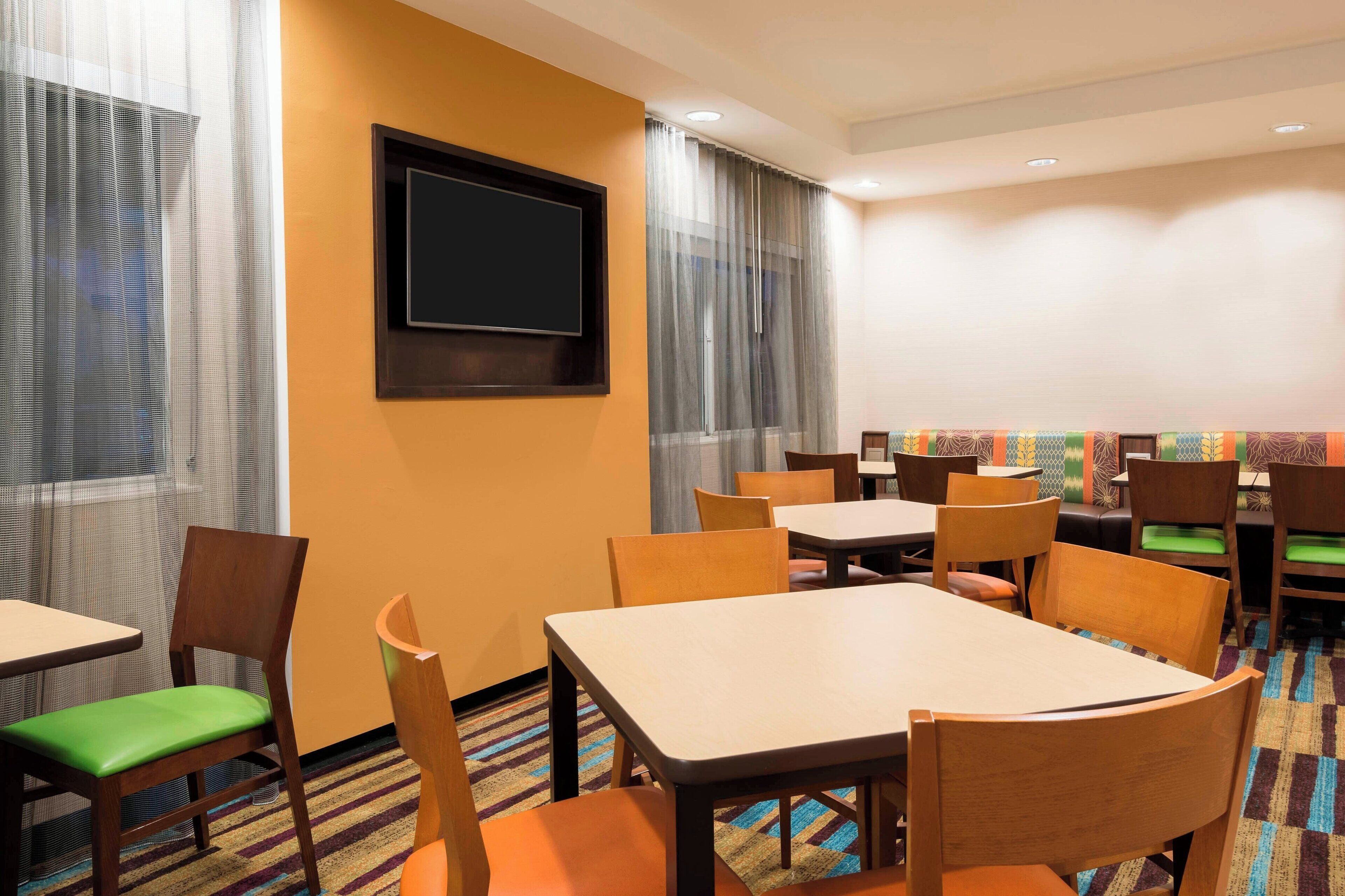 Ein Speisesaal eines Hotels mit Tischen, Stühlen, einem an der Wand befestigten Fernseher und einem gemusterten Teppich.
