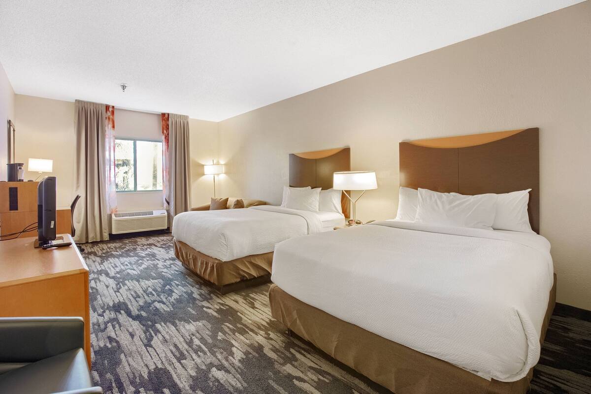 A hotel room with two beds, a desk, a chair, and a television.