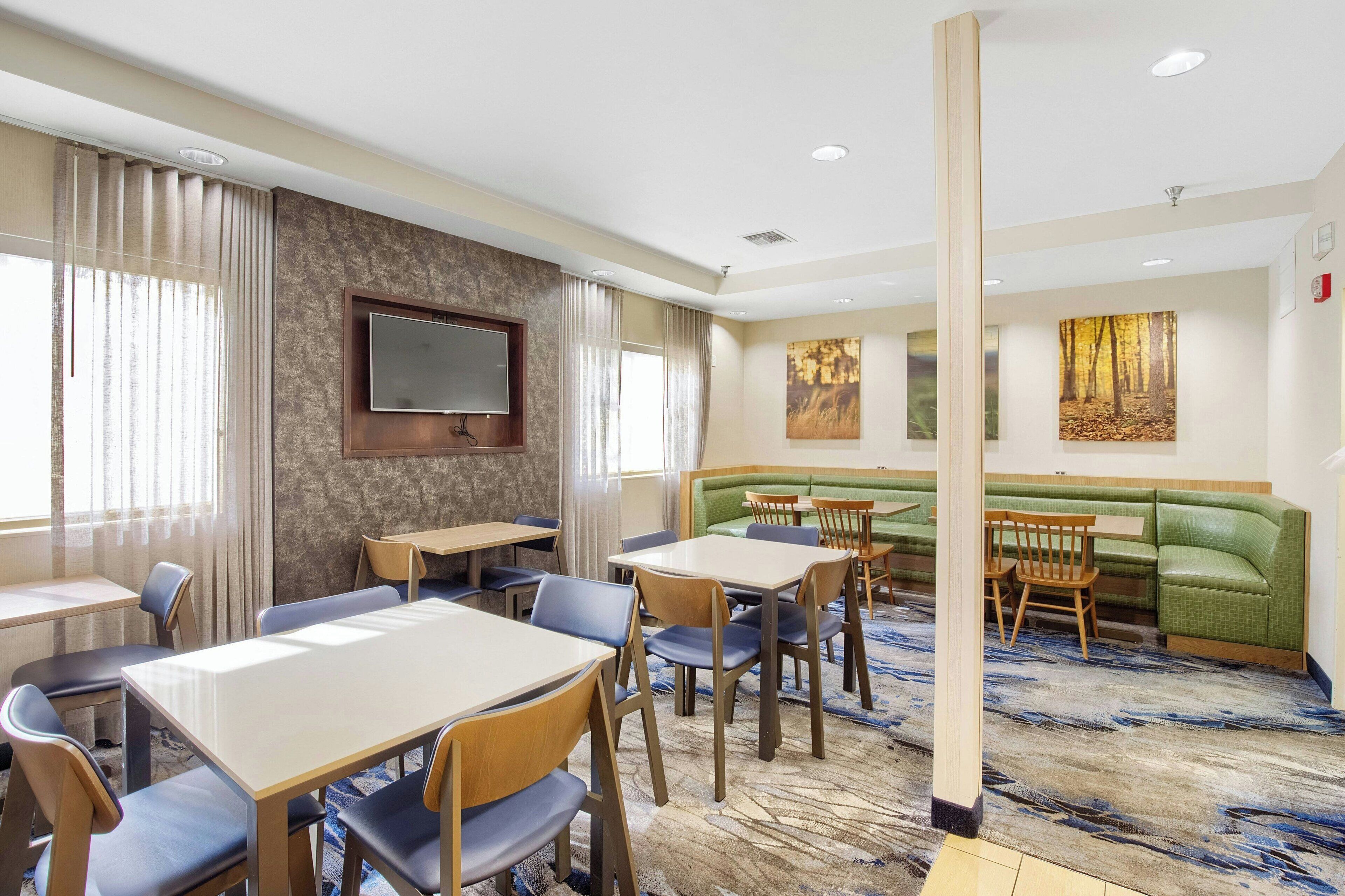 A hotel room with a dining area, a sofa, and a TV mounted on the wall.