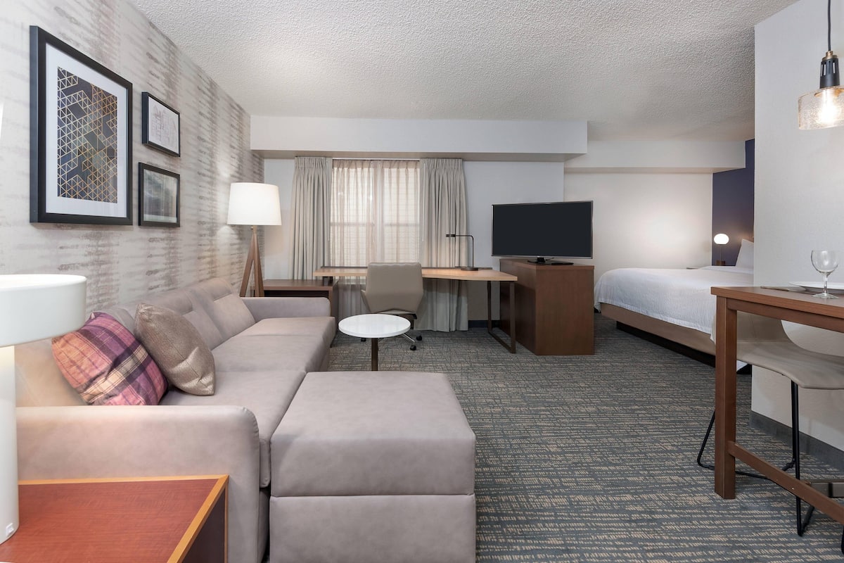 A hotel room with a sofa, a desk, a bed, a TV, and a lamp.