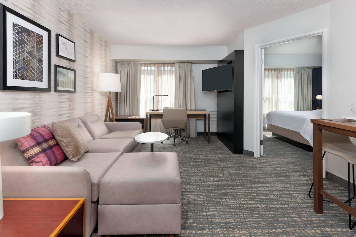 A hotel room with a sofa, a desk, a bed, and a TV.