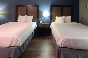 Two single beds with matching headboards and footboards, each with white bedding and a pillow, are positioned in this hotel room.