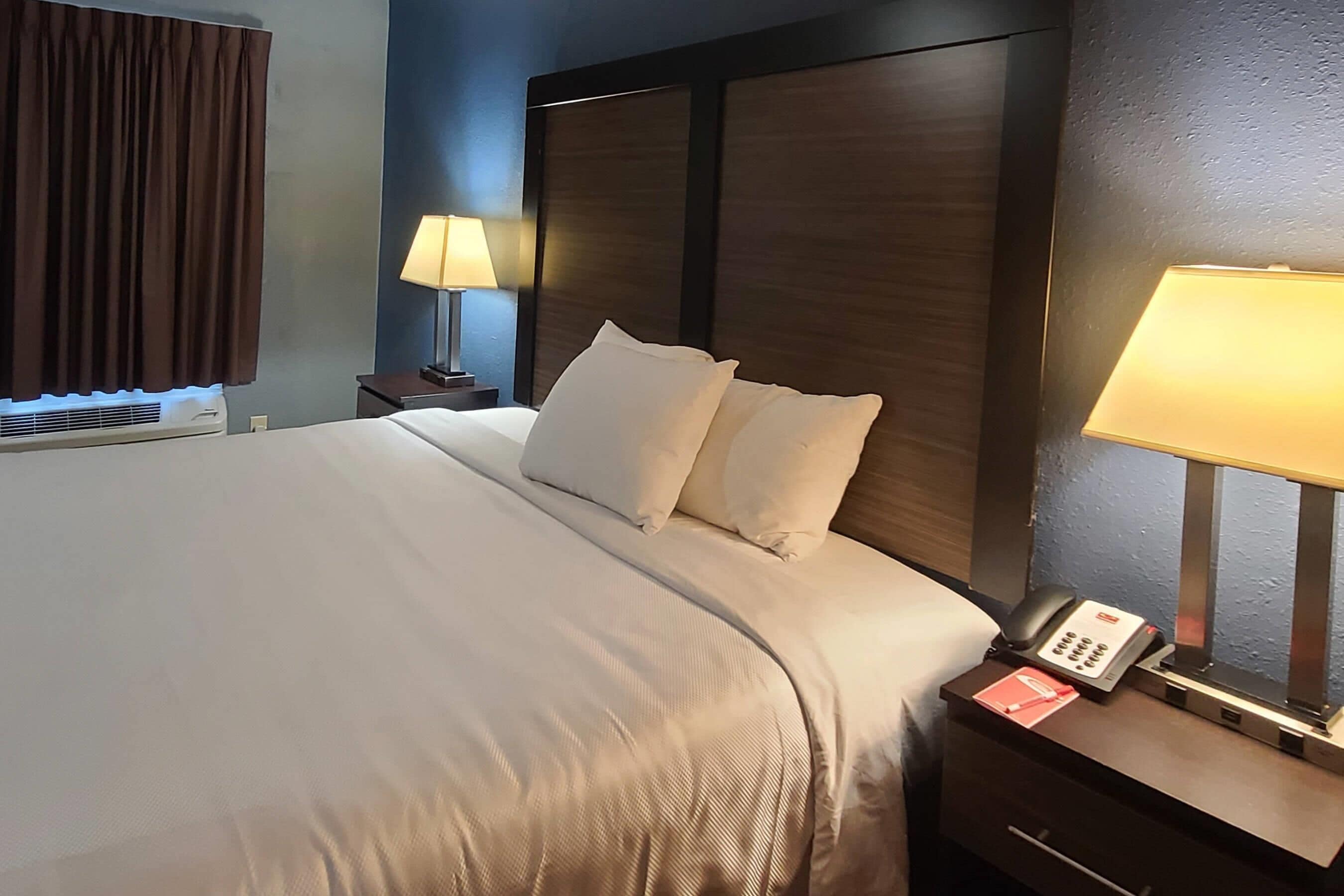 A hotel room with a large bed, a bedside lamp, a phone, and a nightstand.