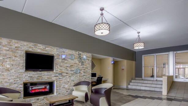 A lobby with a stone wall, a flat-screen TV, a fireplace, and a staircase leading to another level. - Econo Lodge Forest City (Forest City)