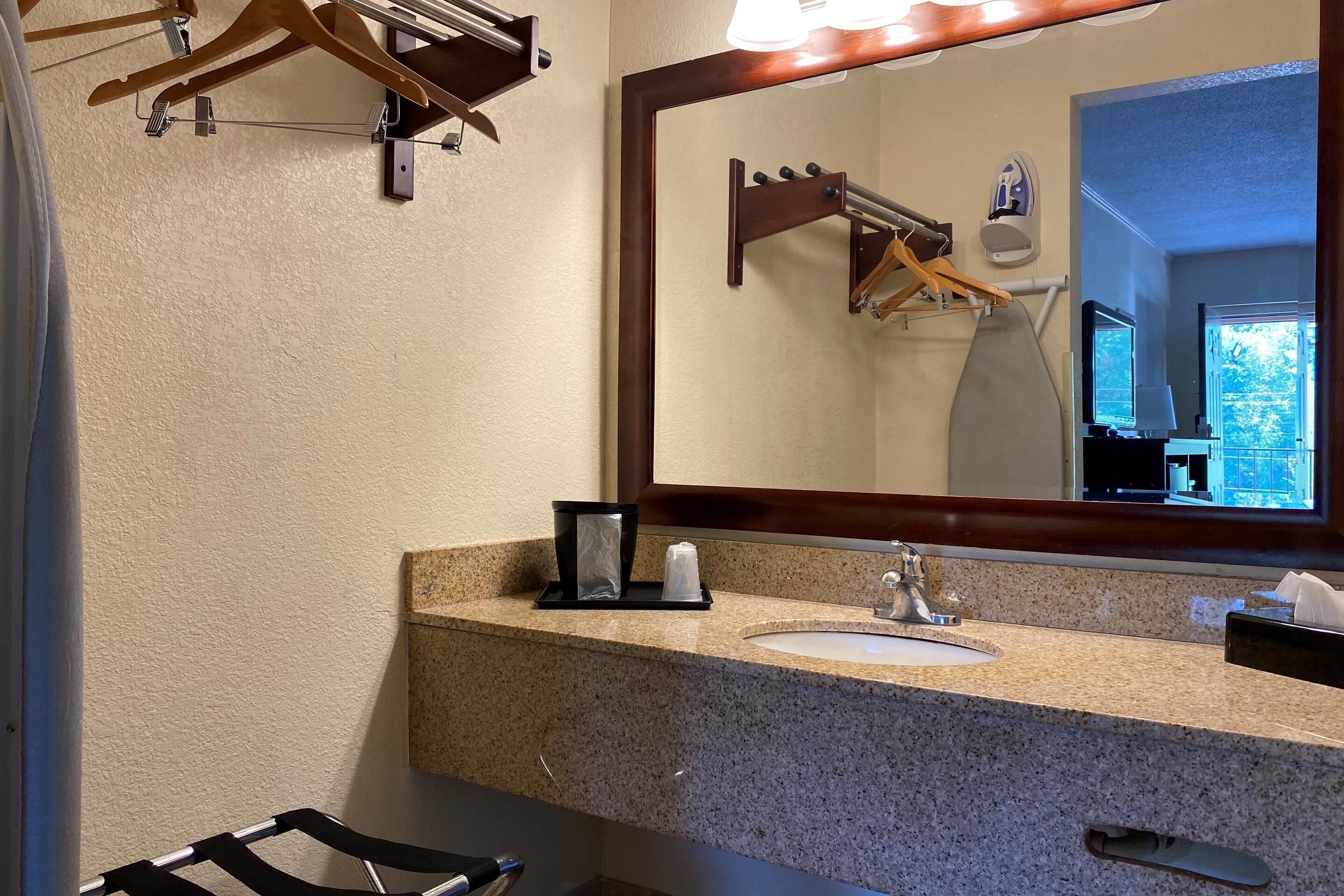 Un baño con encimera de granito, un lavabo, un espejo, dispensador de toallas y un perchero para toallas.