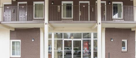 Un bâtiment à deux étages doté d’une entrée en verre, d’un balcon avec des rampes en métal et d’une façade en briques.