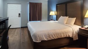 A hotel room with a large bed, a desk, a chair, a door, a window with curtains, and a bedside lamp. - Econo Lodge Forest City (Forest City)