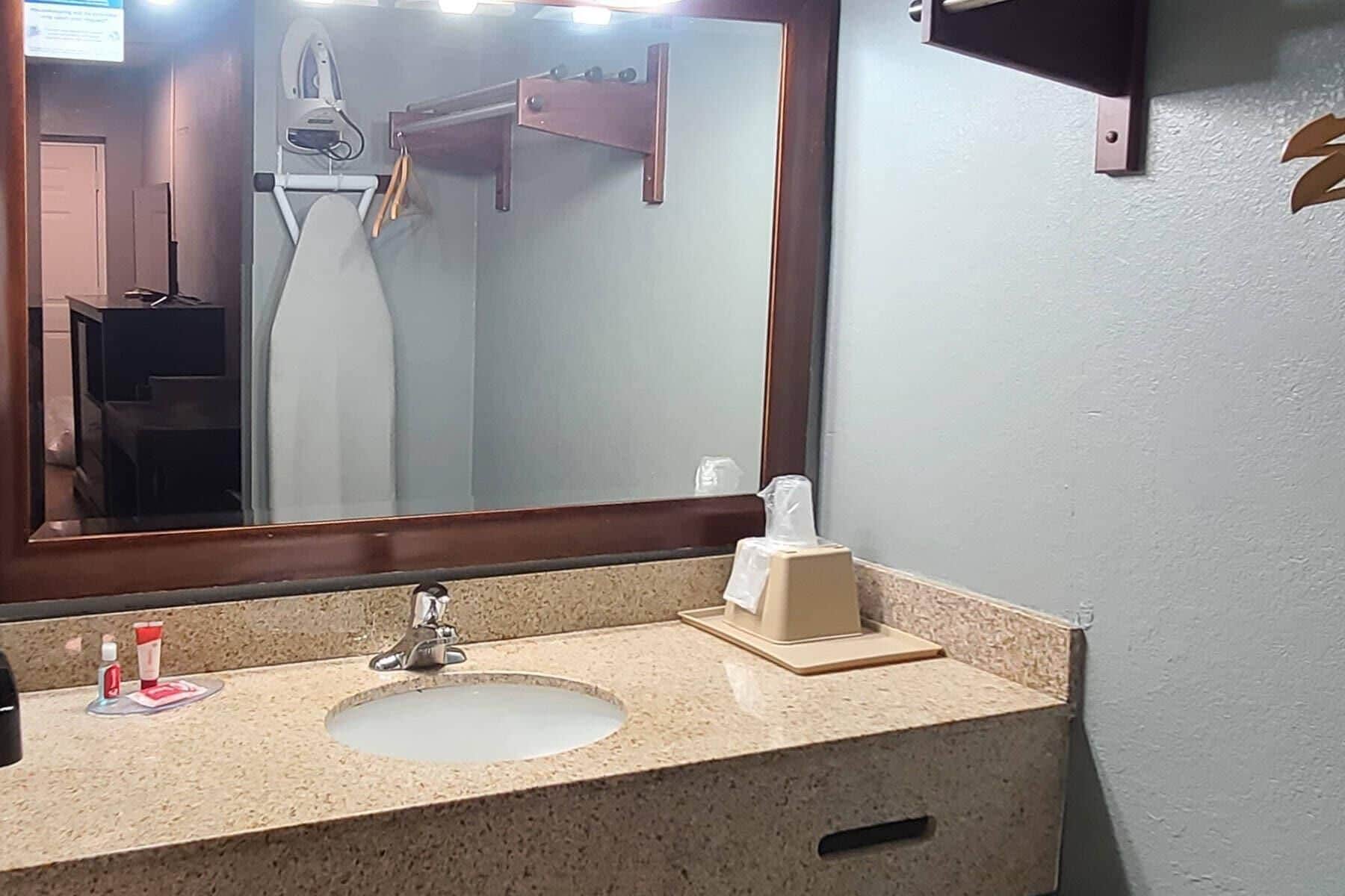 A bathroom with a sink, mirror, towel rack, and a soap dispenser.