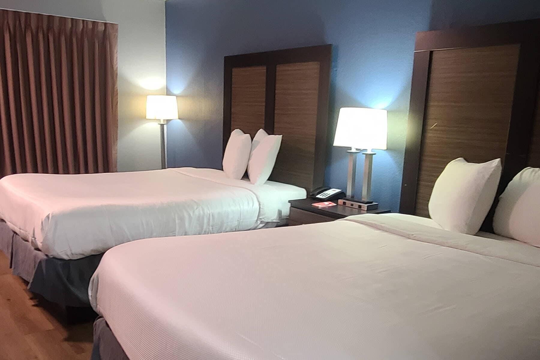 A hotel room with two beds, a nightstand with a lamp, and a telephone.