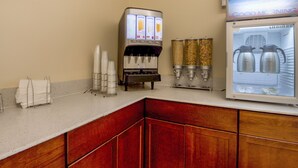 A kitchenette with a coffee machine, a beverage dispenser, and a refrigerator with milk dispensers. - Econo Lodge Forest City (Forest City)