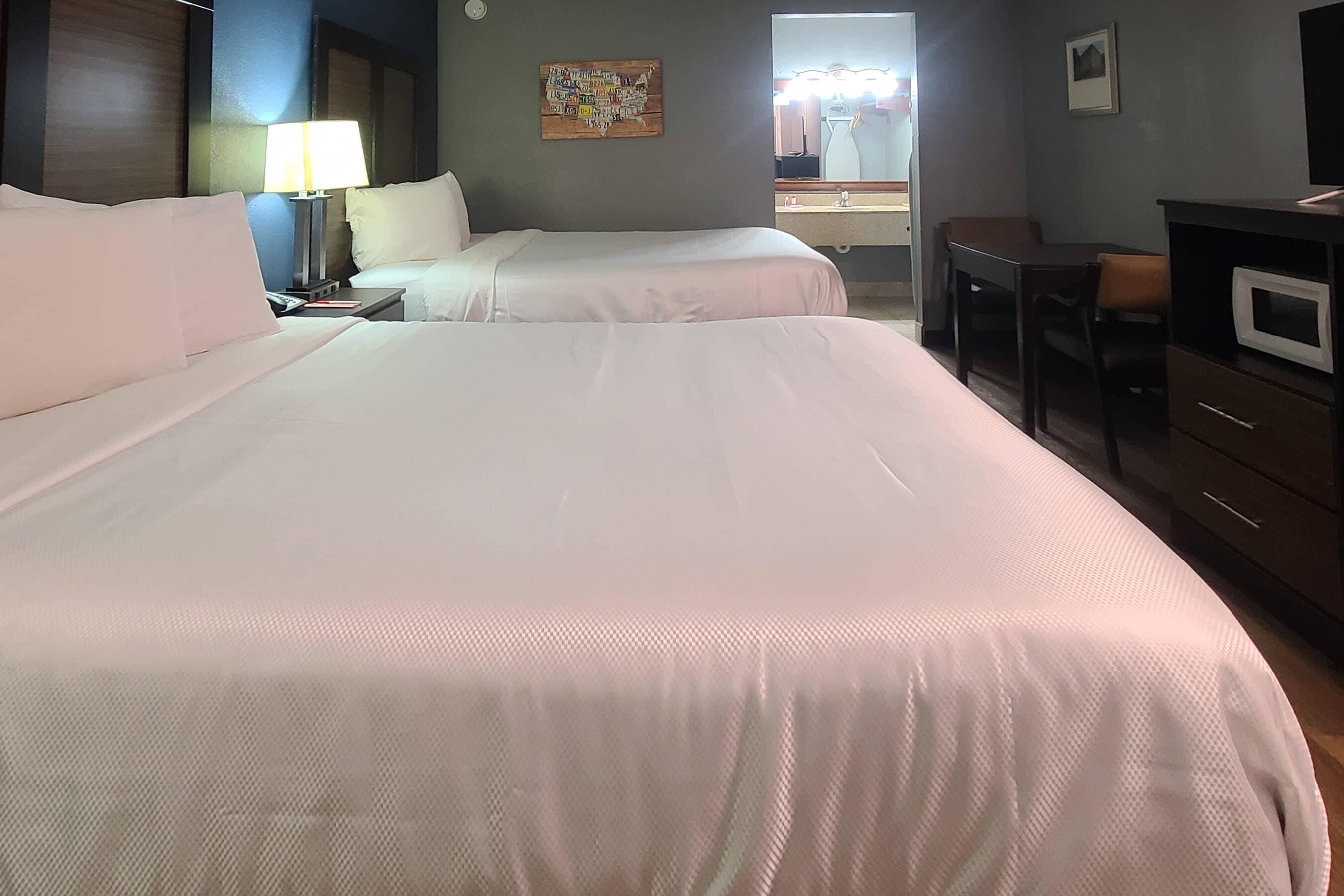 A hotel room with two beds, a desk, a chair, a TV, and a microwave.