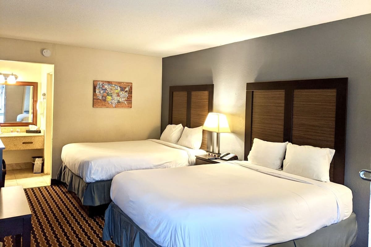 A hotel room with two beds, a bathroom, a desk, and a wall-mounted map.