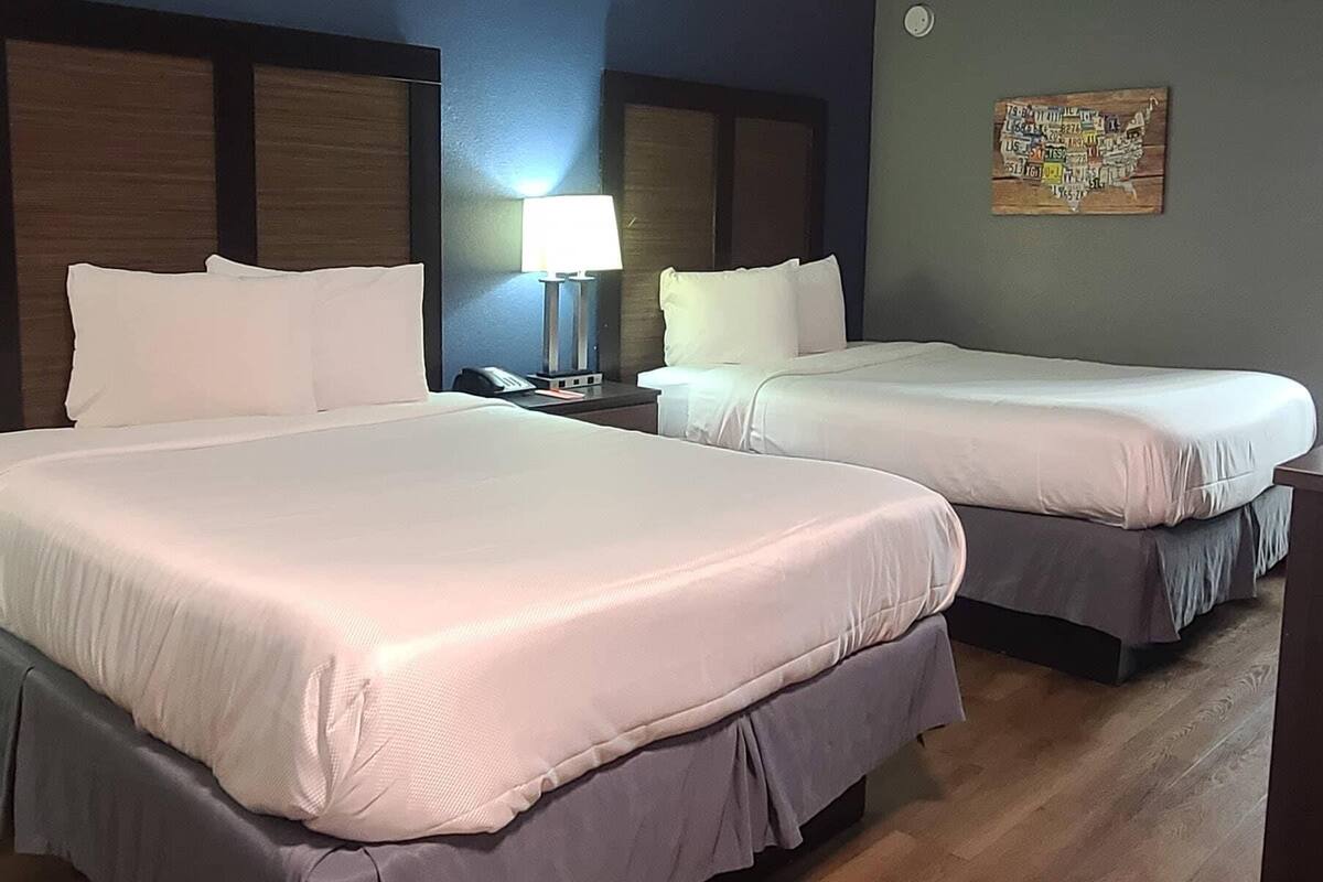 Two beds with white linens, a nightstand with a lamp, and a wall with a map.