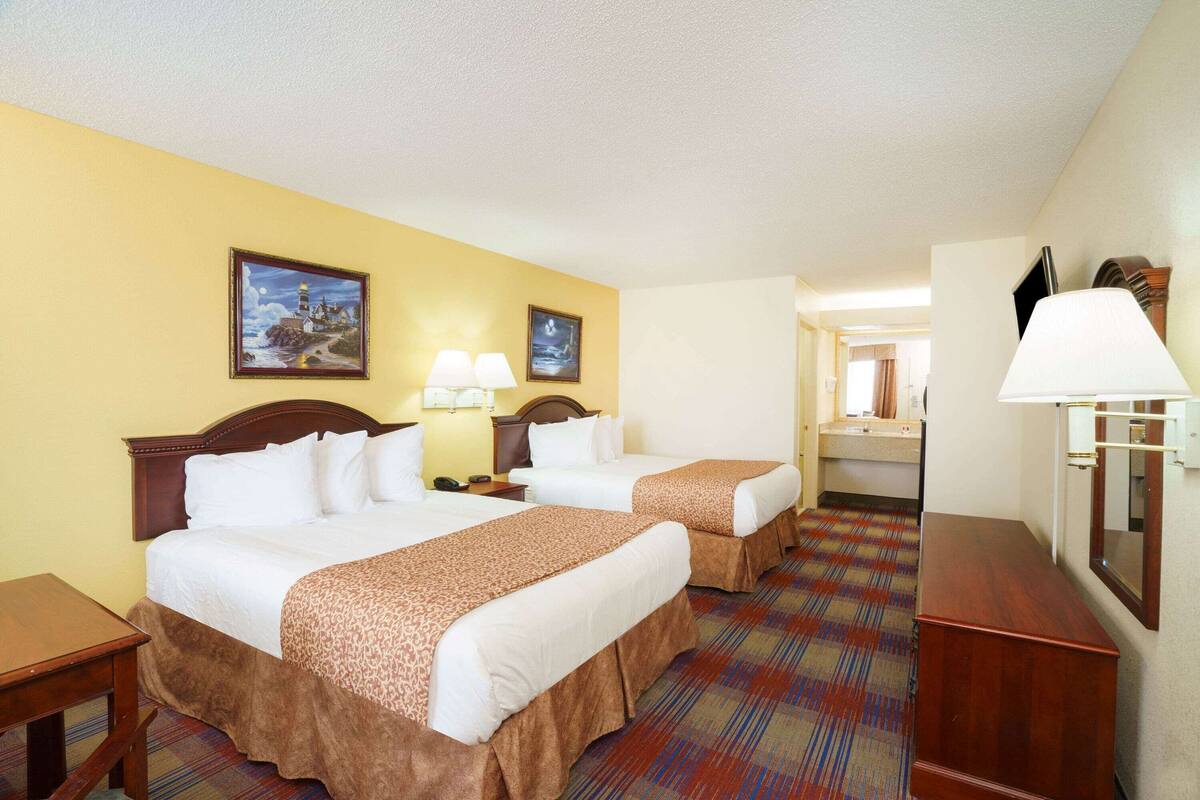 Una habitación de hotel con dos camas, un tocador de madera, un espejo y una lámpara.