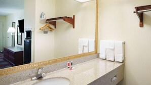 Une salle de bain avec un lavabo doté d’un plan de travail en granit, un miroir et deux serviettes suspendues à un porte-serviettes.