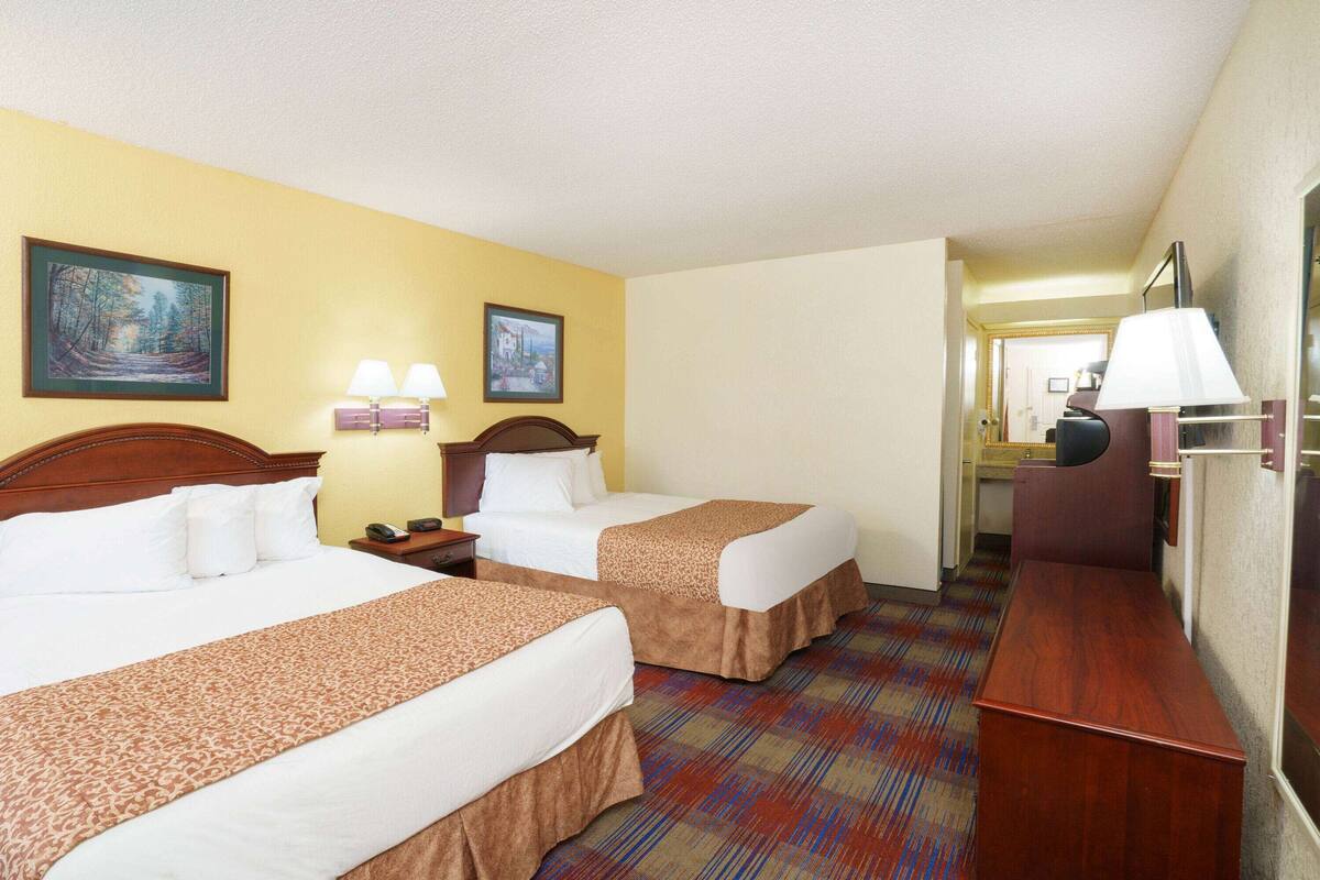 Habitación de hotel con dos camas, un escritorio, una silla y una lámpara.