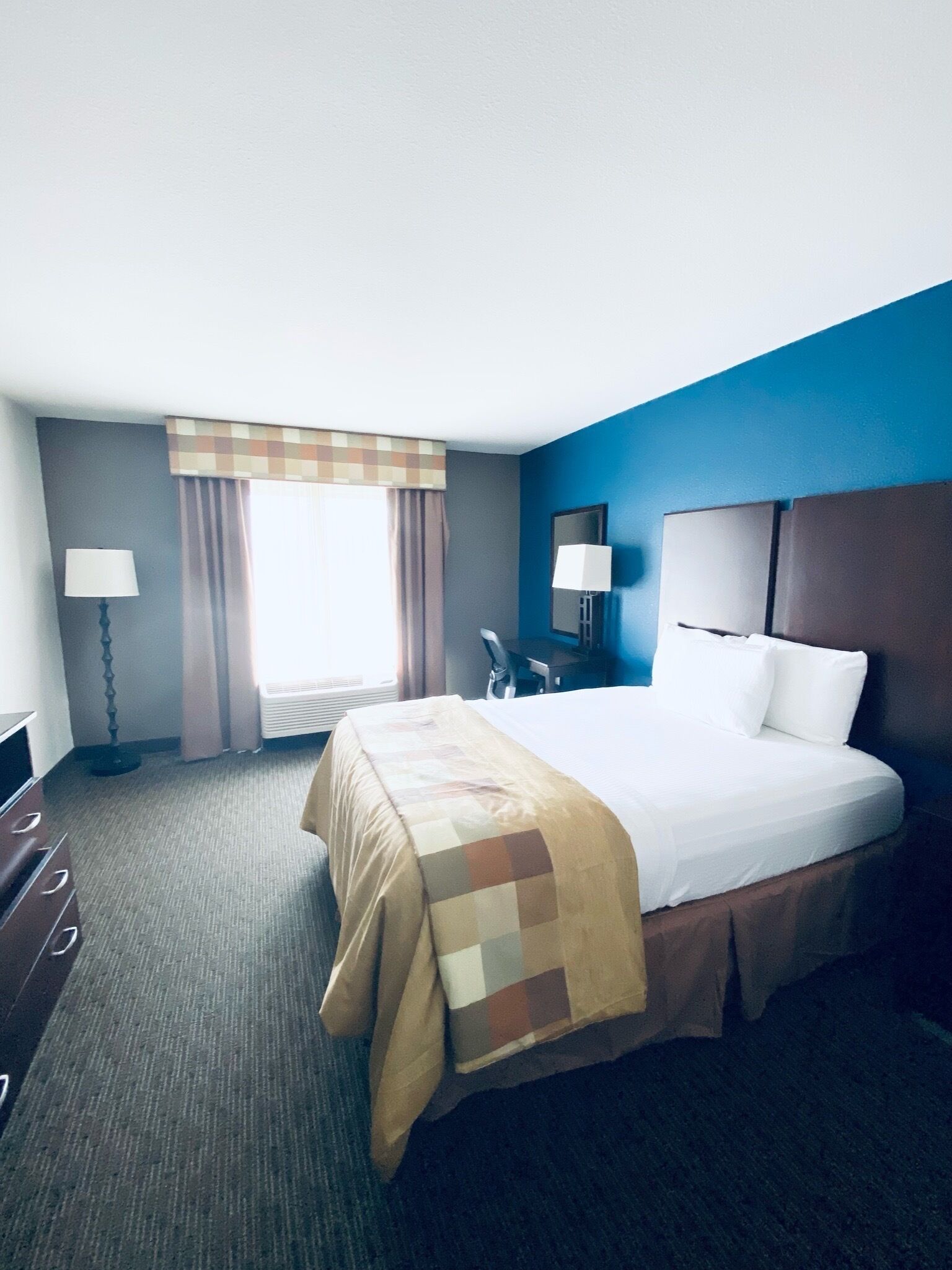 Une chambre d’hôtel avec un grand lit, un bureau, une chaise, une lampe et une fenêtre avec des rideaux.