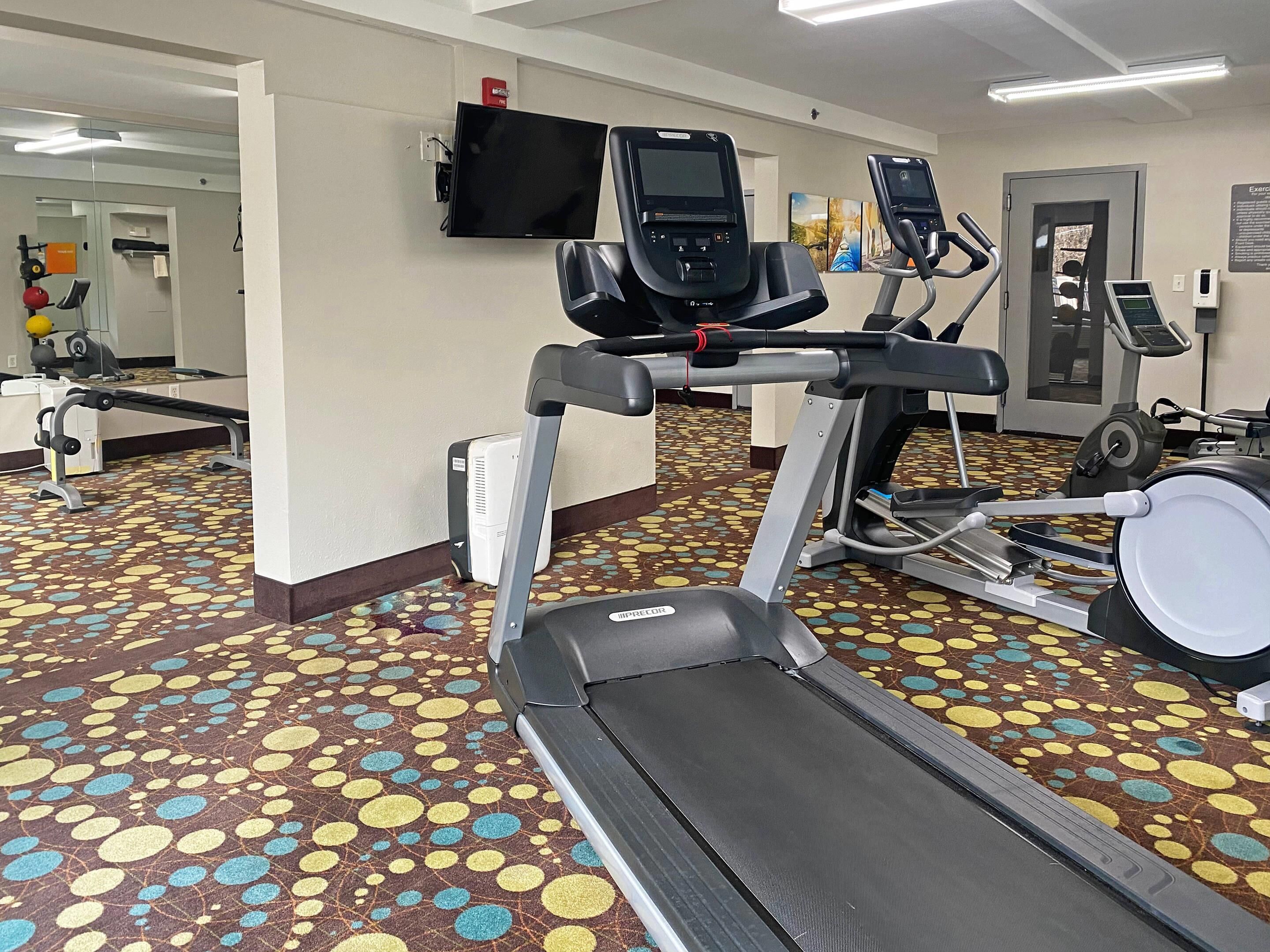 Un gimnasio con cintas de correr, bicicletas estáticas y un espejo grande.
