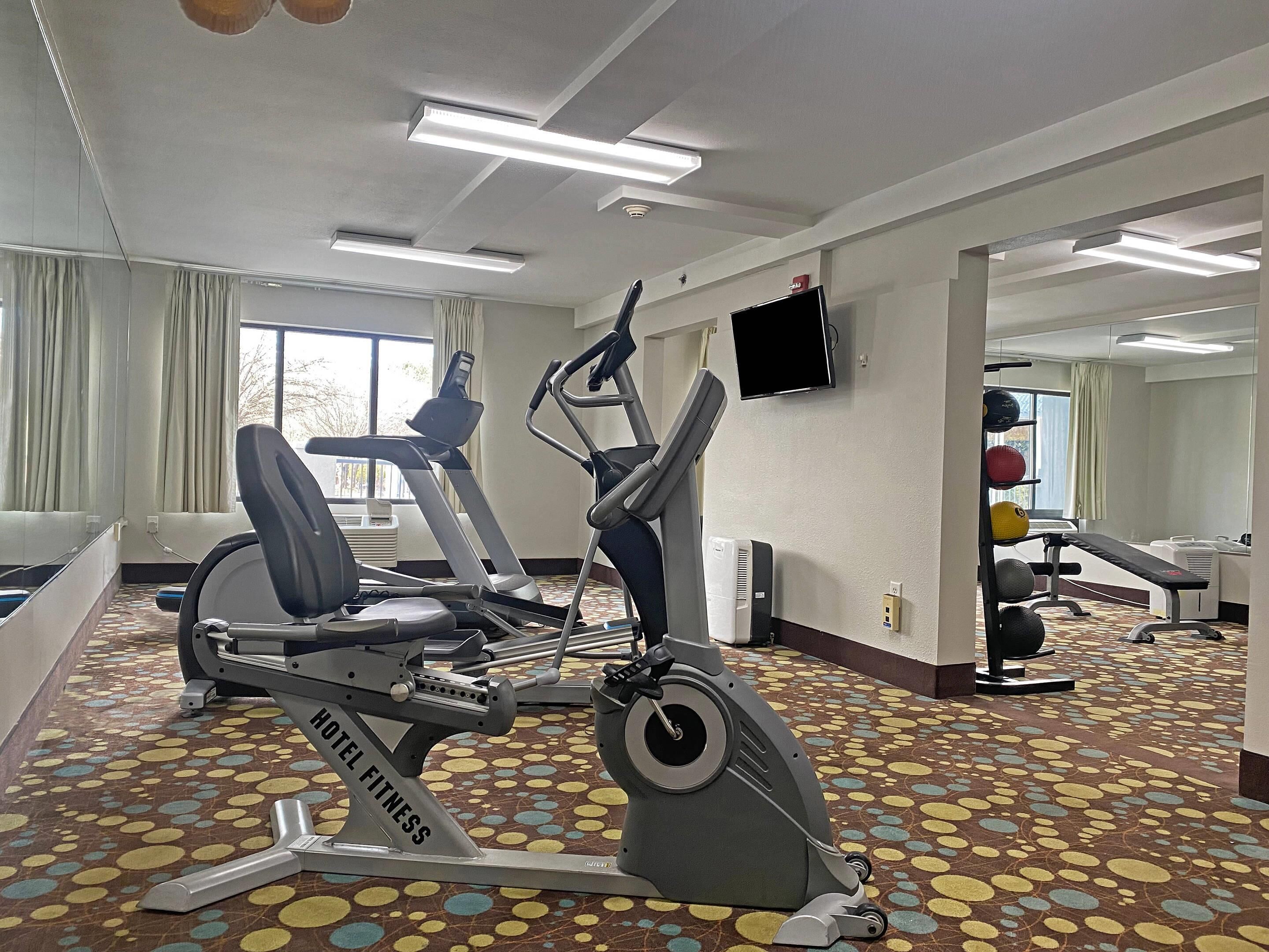 Een hotel fitnessruimte met trainingsapparatuur, een televisie en een kamerbreed tapijt met dessin.