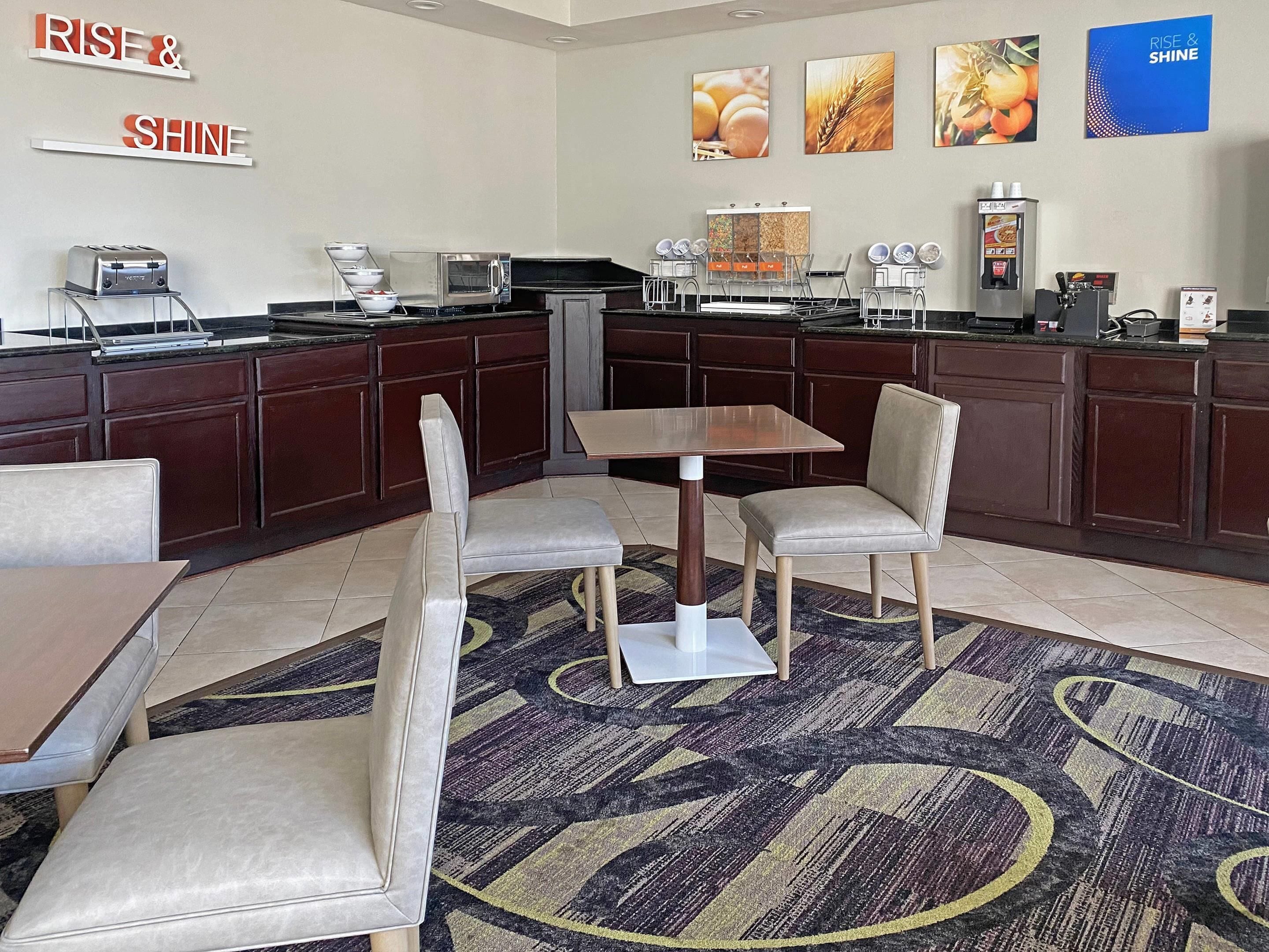 A hotel kitchen with a buffet setup, a coffee machine, and a seating area with a table and chairs.