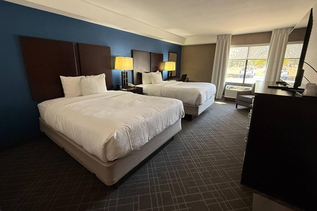 A hotel room with two beds, a desk, a chair, and a large window with a view.