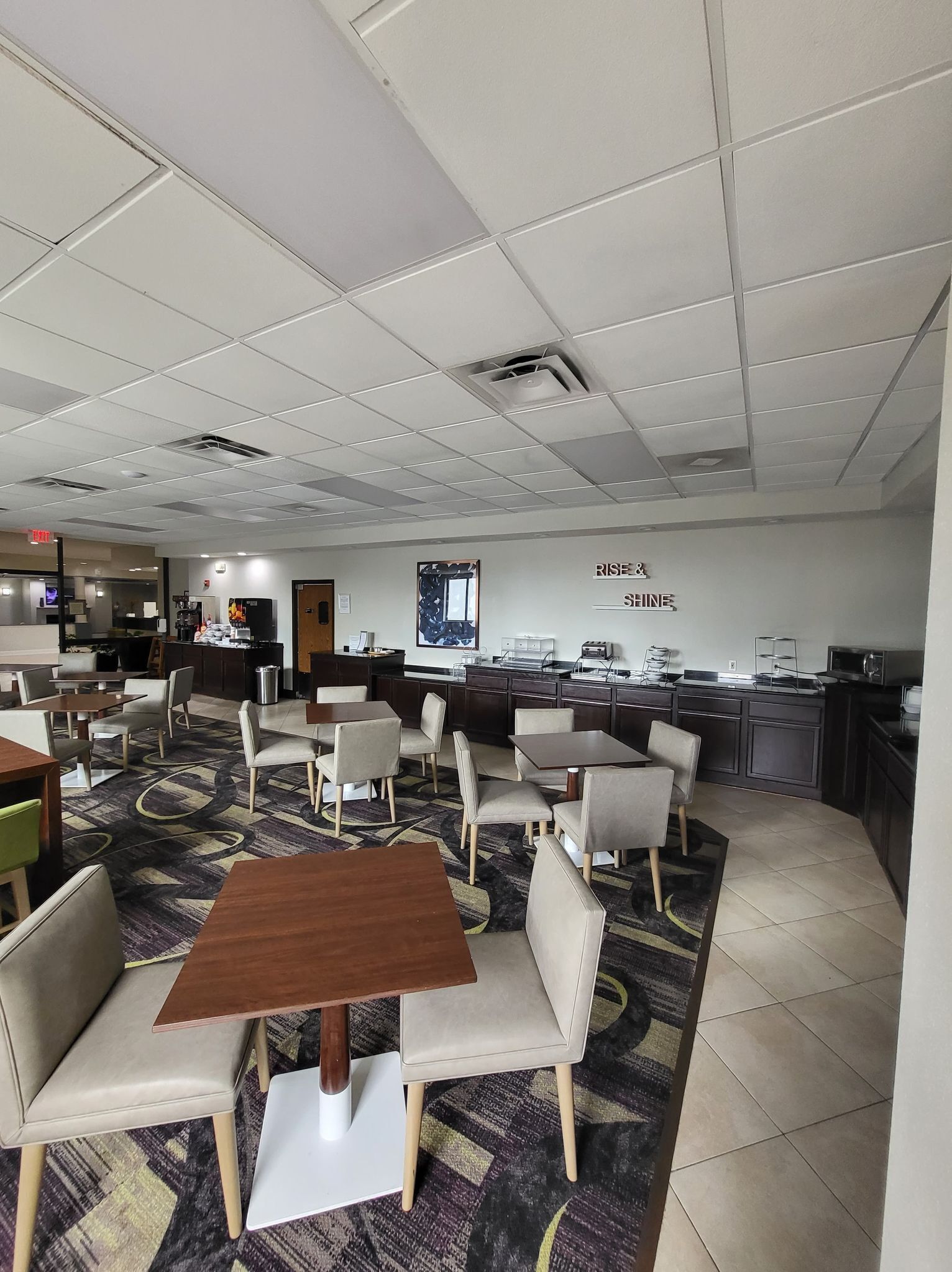 A modern hotel lobby with a reception desk, seating area, and a kitchenette.