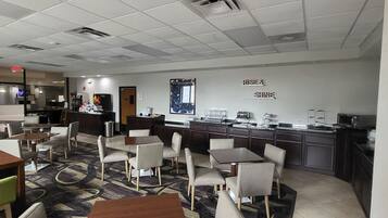 A modern hotel lobby with a reception desk, seating area, and a kitchenette.