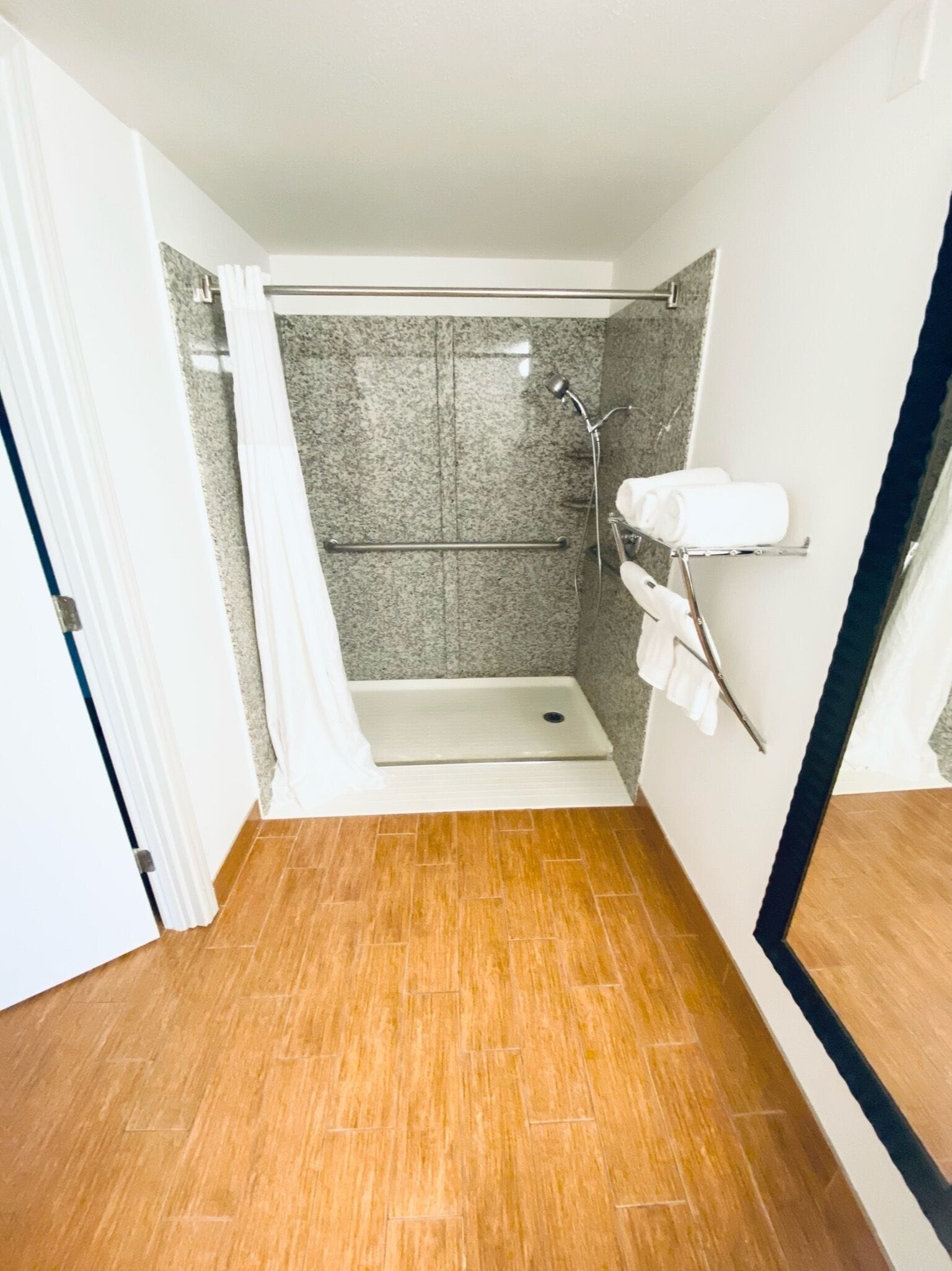 Un baño pequeño y estrecho con ducha, un perchero y suelo de madera.