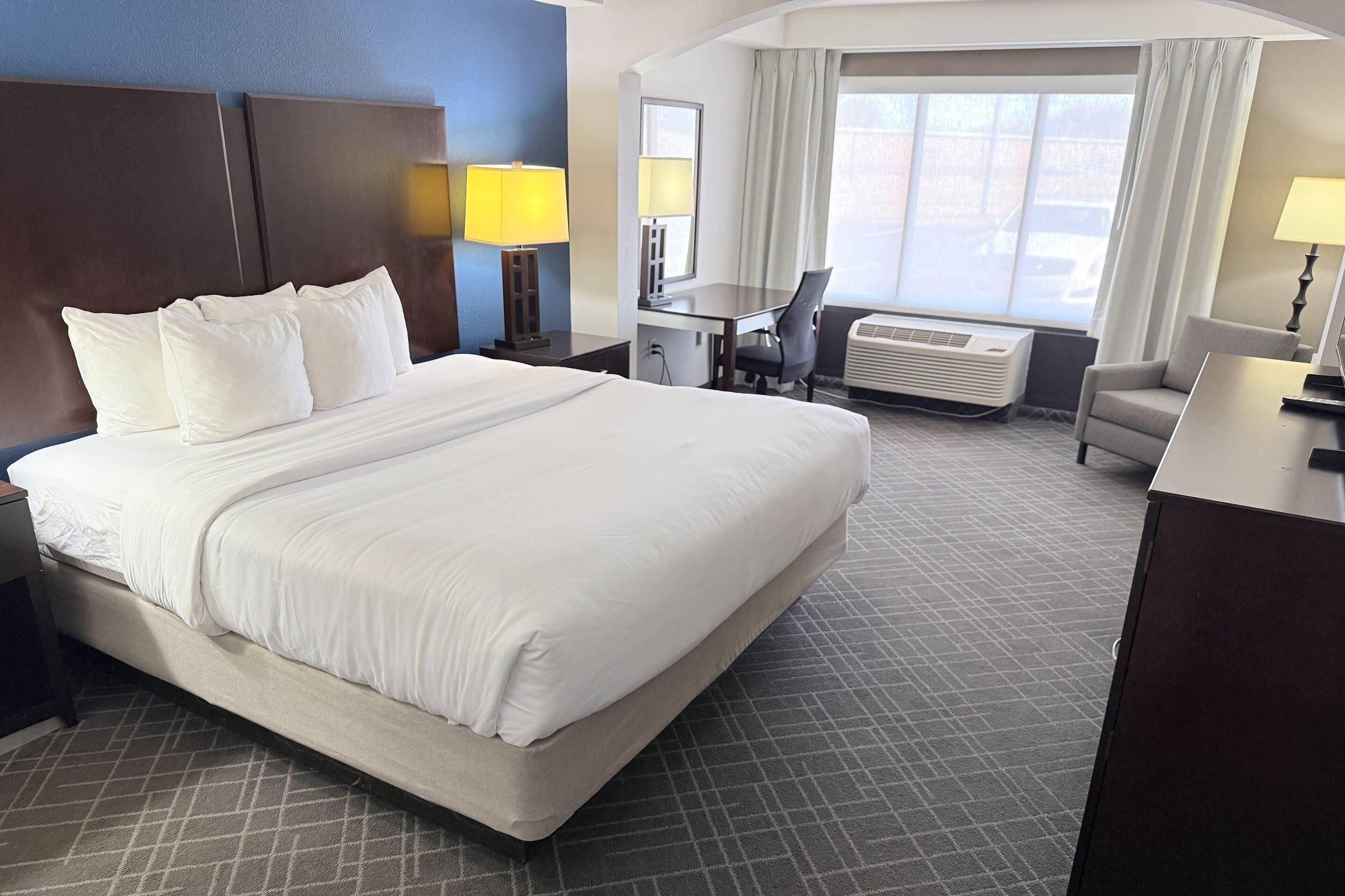 A hotel room with a large bed, a desk, a chair, a lamp, and a window with curtains.
