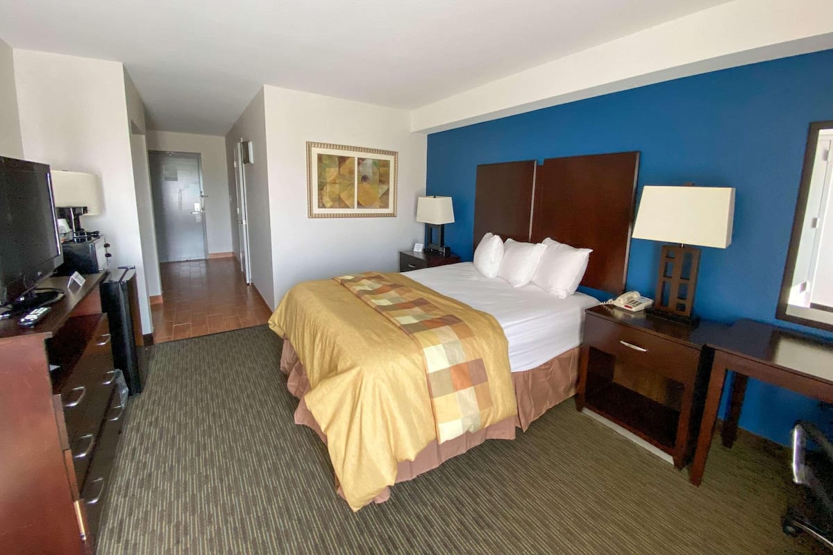 A hotel room with a bed, a desk with a computer, a TV, a telephone, and a lamp.