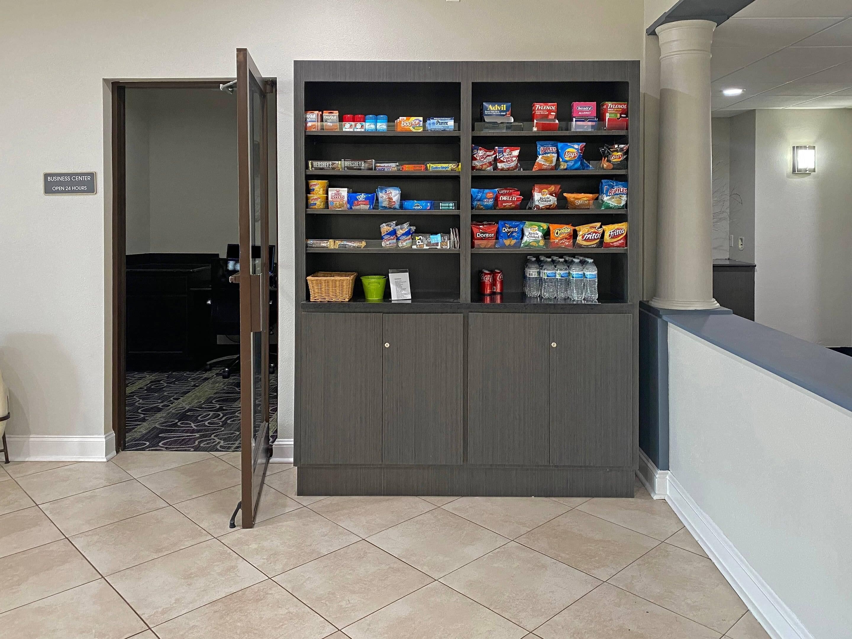 Un mueble de almacenamiento con aperitivos y bebidas, un letrero de centro de negocios y un piso de baldosas.