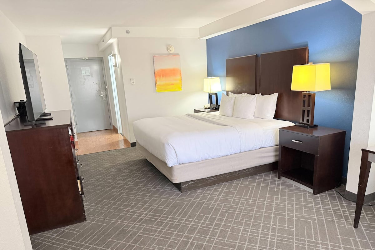 A hotel room with a bed, bedside lamps, a desk, a TV, and a door.