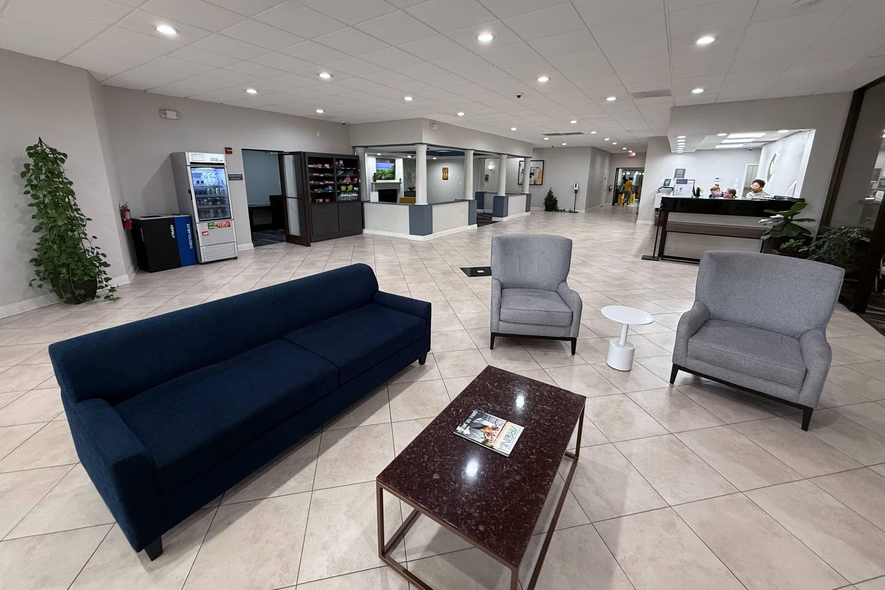 Una hall con un divano blu, due poltrone, un tavolino da caffè, una macchina per distributore e una reception.