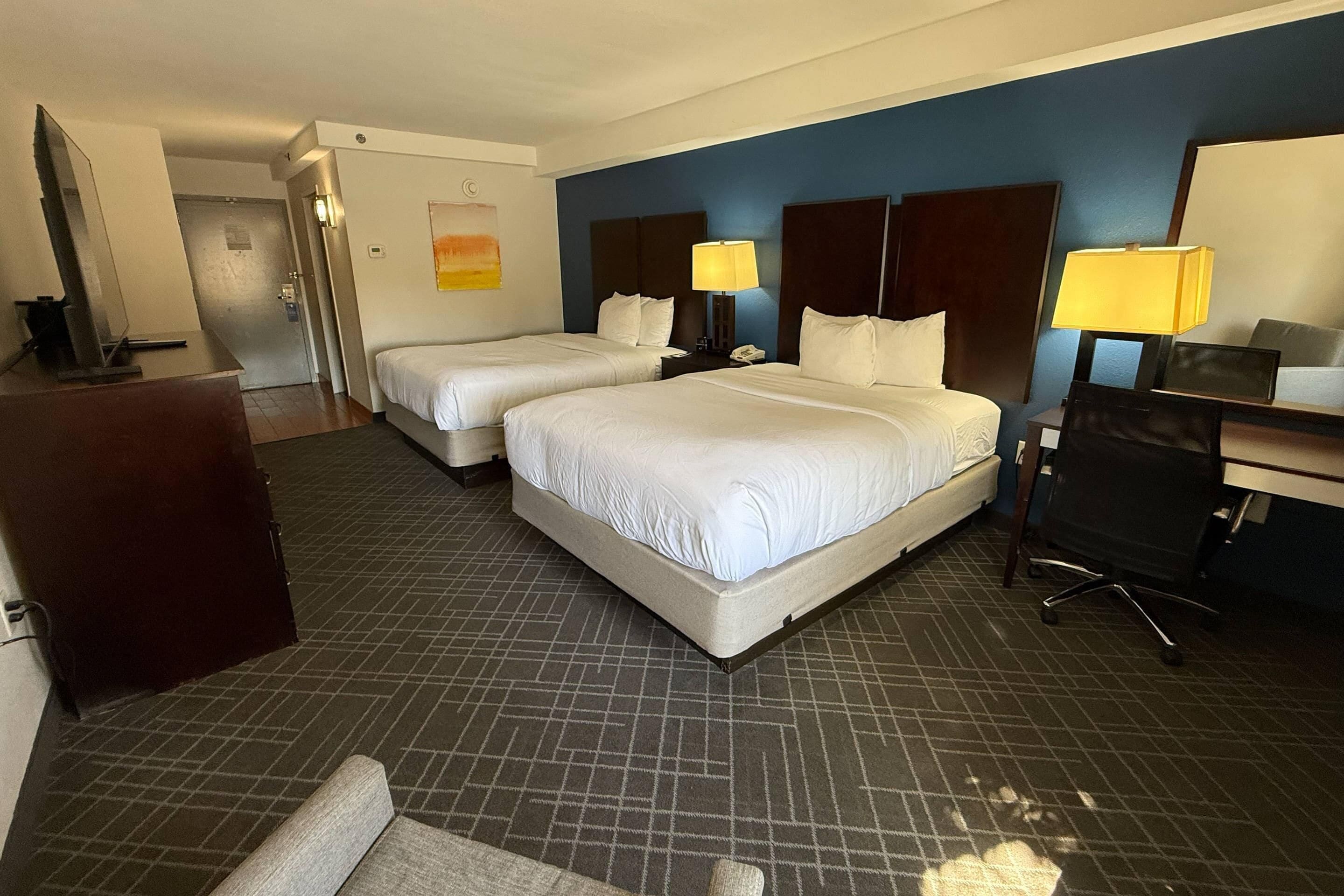 Una habitación de hotel con dos camas, un escritorio, una silla y una lámpara de escritorio.