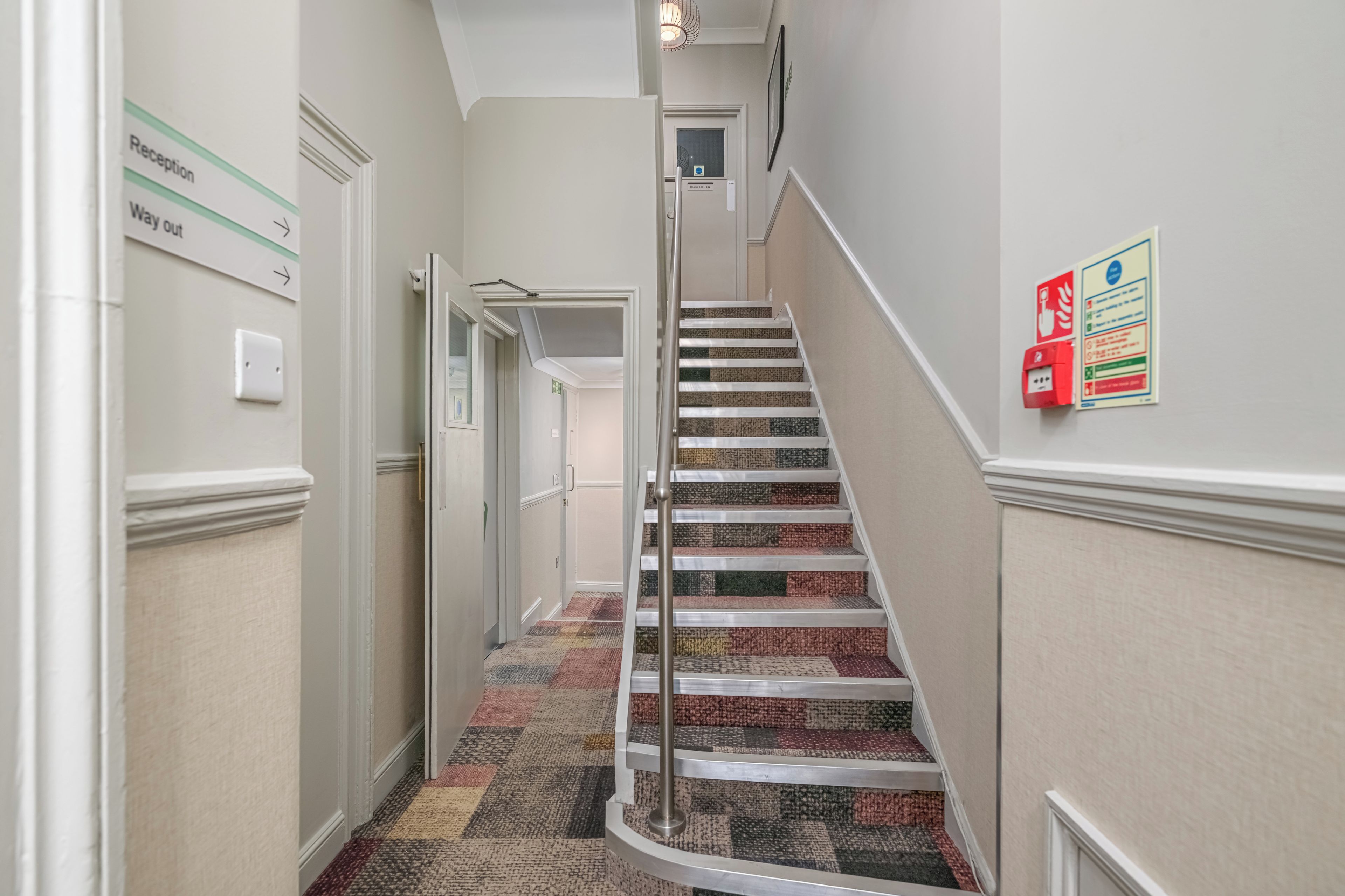 A hallway with a carpeted staircase, a reception sign, and a fire safety sign.